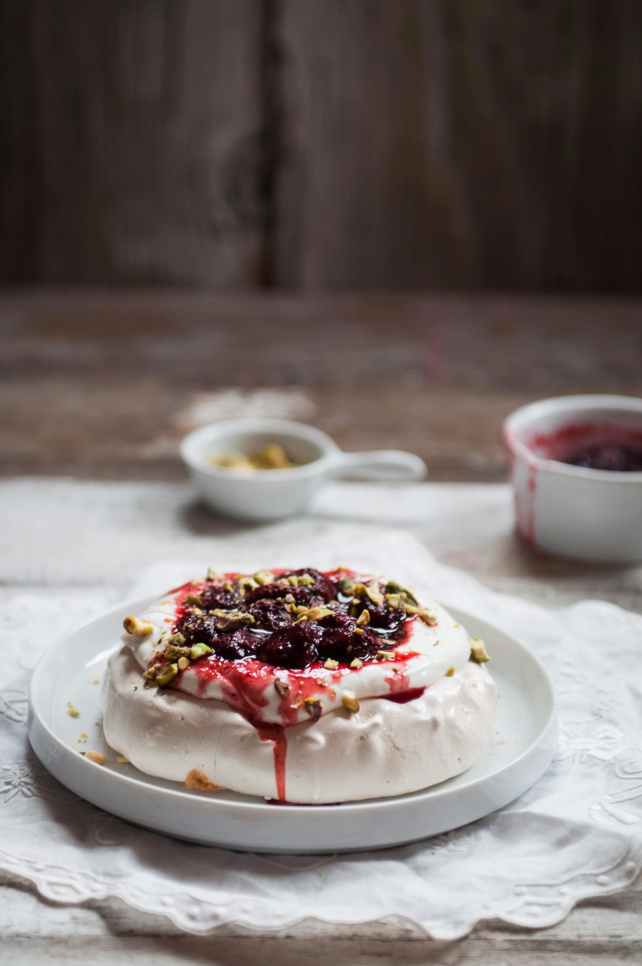 A cardamom pavlova topped with strained yogurt sweetened with honey and fresh strawberry compote and sprinkled with pistachios to finish.