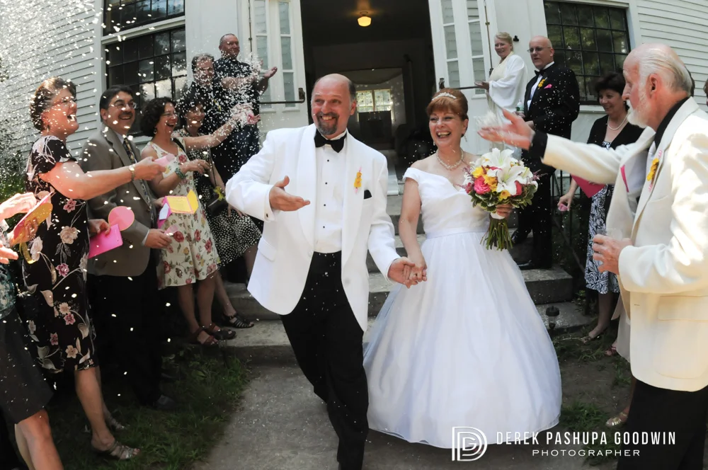 The bride and groom exit the church surrounded by family throwing rice