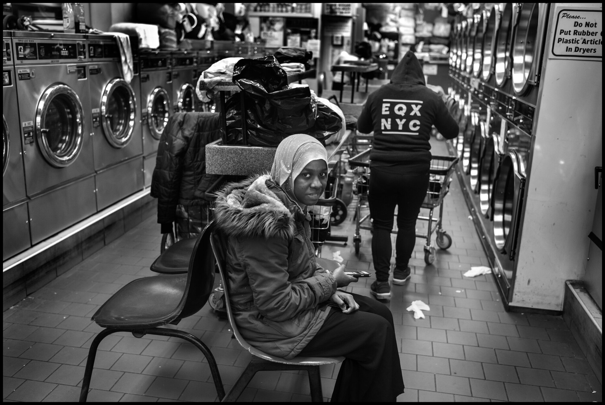  Diallo, a young woman from Guinée, waits for her washing to finish at a laundromat on Amsterdam Ave.  March 23, 2020. © Peter Turnley.  ID# 02-008 