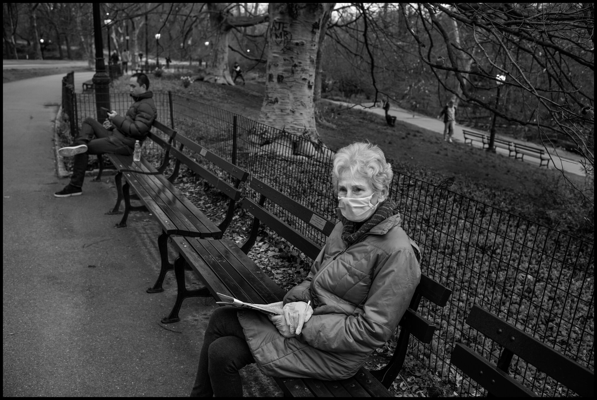  Sally sits doing crossword puzzle in Central Park. I asked her how she was making it, and she replied, “I have a few other challenges-my husband is going through a 6 month therapy for another health issue.”  March 31, 2020. ©Peter Turnley.   ID# 09-