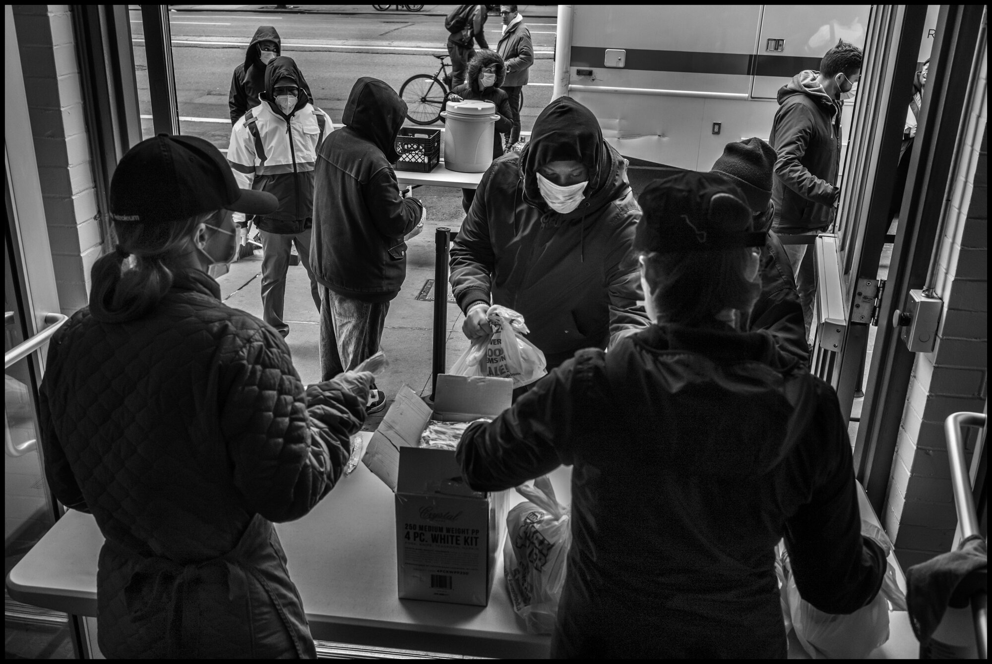  Volunteers hand out bags of food to people in need of food at The Bowery Mission, New York City.   April 10, 2020. © Peter Turnley  ID# 18-004 