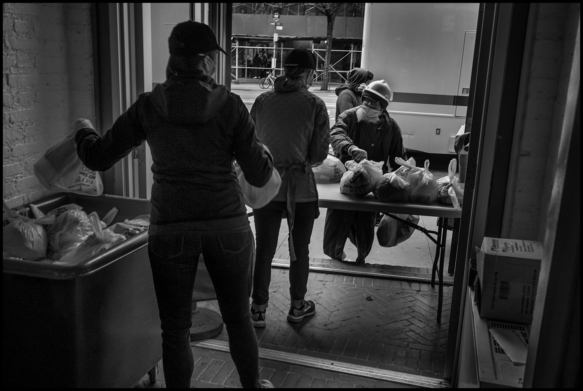  A person, one of hundreds homeless or without means to buy food at this time, that had stood in line in the cold, walks up to receive a bag of food at lunch time from volunteers at The Bowery Mission.   April 10, 2020. © Peter Turnley  ID# 18-010 