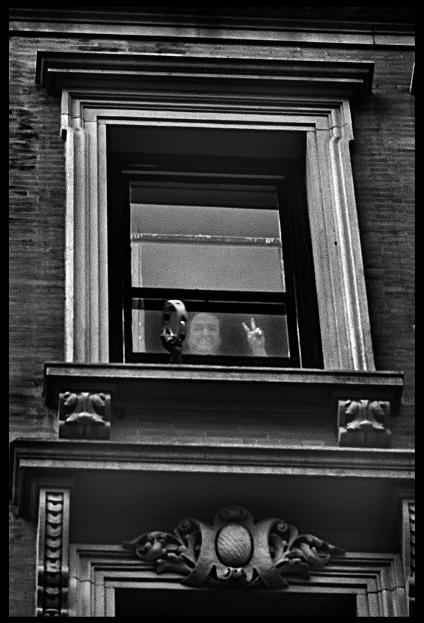  An elder person, making a peace sign from a window in the Upper West Side.  April 12, 2020. © Peter Turnley  ID# 19-003 