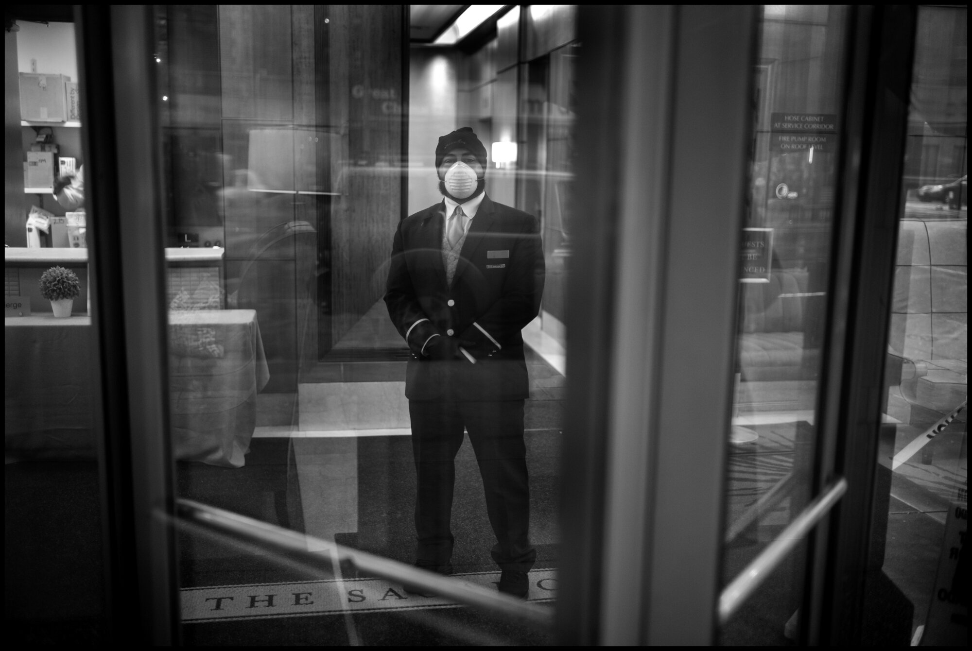  A doorman stands proudly with his uniform and protective mask at a building on the Upper Westside.   March 23, 2020. © Peter Turnley.   ID# 02-004 