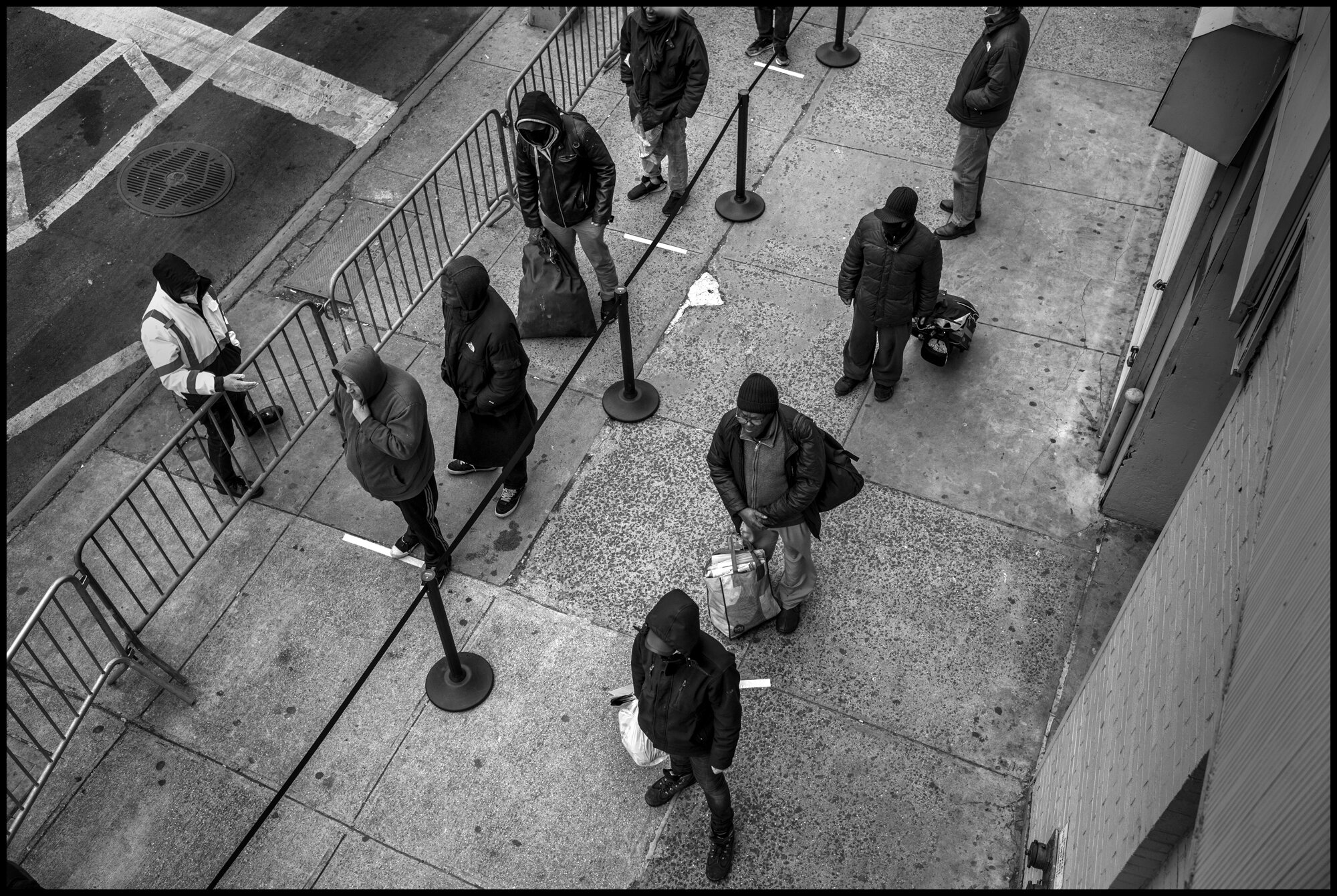  People stand in line waiting for food at The Bowery Mission in New York City.   April 10, 2020. © Peter Turnley.   ID# 18-019 