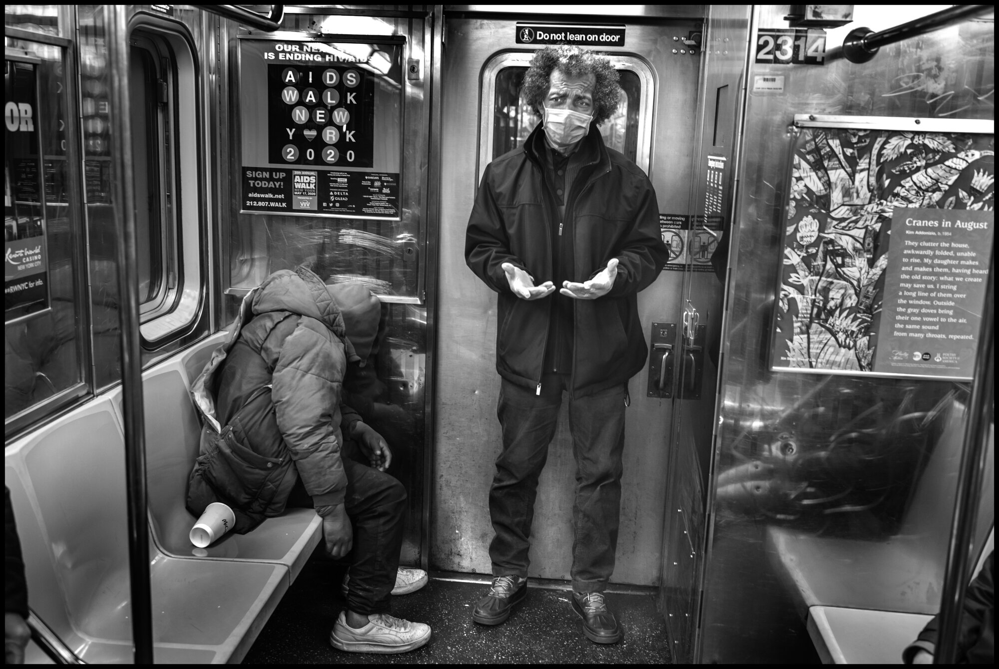  Harry, 63, stands at the back of a subway car next to a homeless man that has taken shelter in the train. I ask him what he does in life and he replied, “I just try to help out.”   March 26, 2020 ©Peter Turnley.   ID# 04-007 