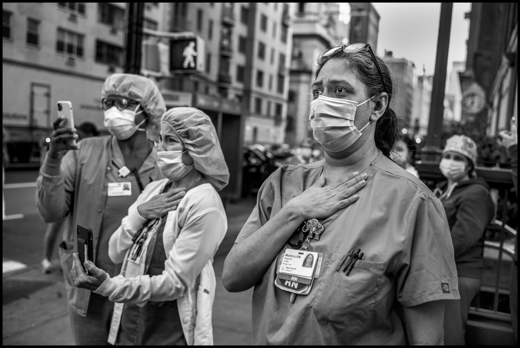  Simi, Erika, and Monica listen with great emotion as a young man sings from atop a car, “America the Beautiful”, at 7pm on Mother’s Day.   May 10, 2020. © Peter Turnley.   ID# 42-003 