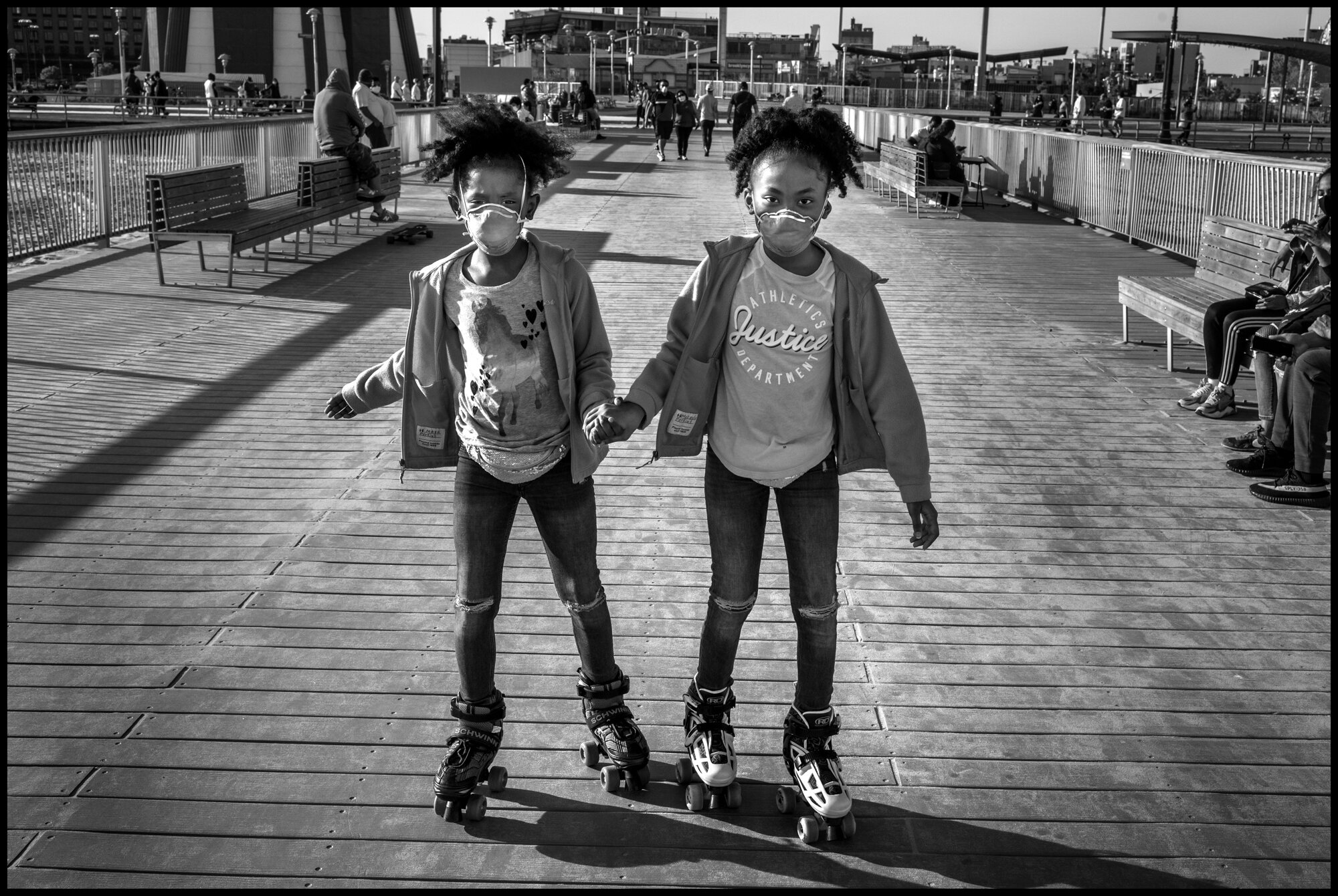  Two young sisters, Maya and Makayla, 8 and 9 years old, roller skated down the pier with their masks on. Their parents told me this was their first time out to Coney Island since the crisis began.   May 16, 2020. © Peter Turnley.  ID# 49-004 