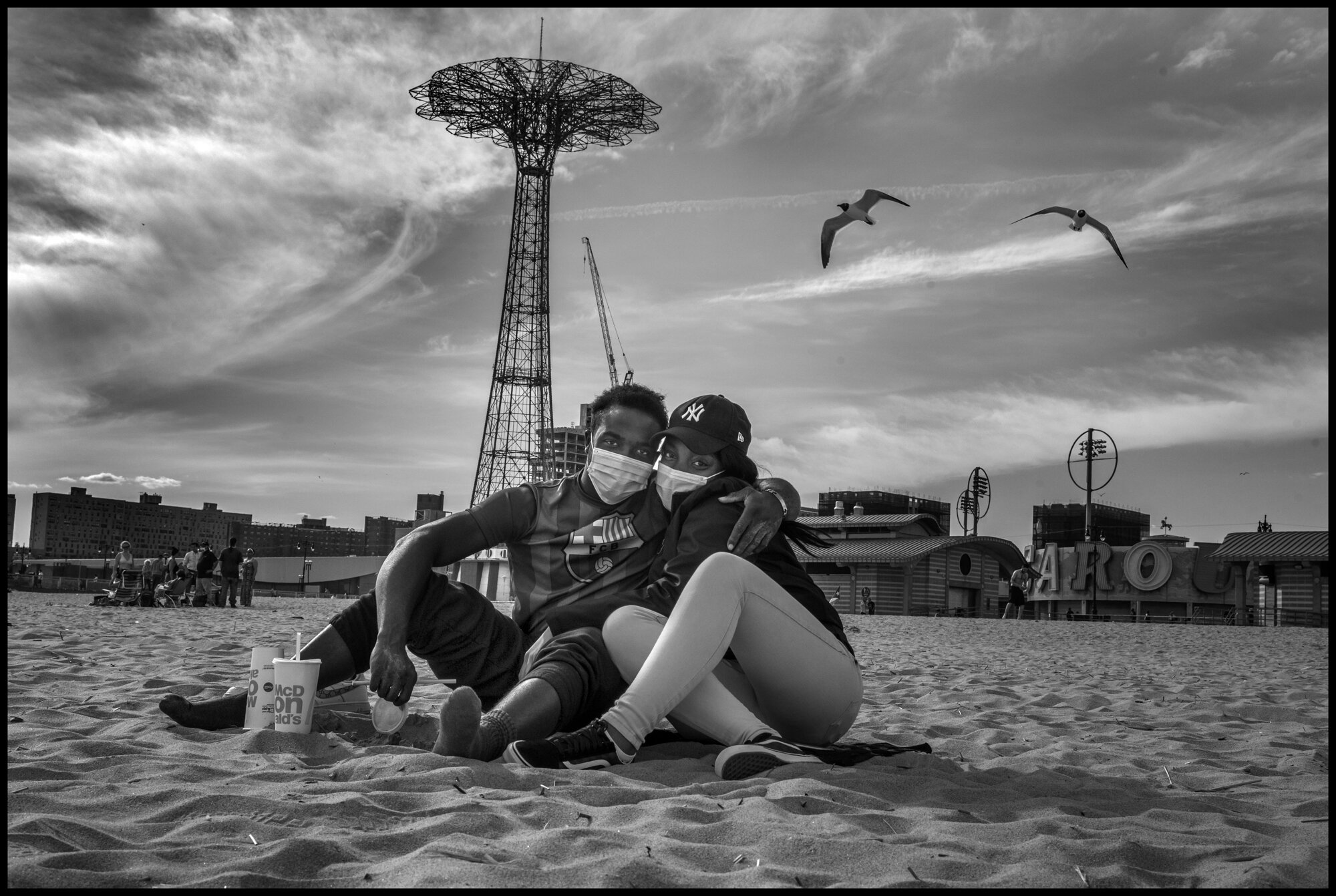  George and Regina, both born in Haiti, have known each other for a long time-but their romance is young, and they sat, both masked, clearly joyful to be outside, and together. Coney Island, Brooklyn, New York.  May 16, 2020. © Peter Turnley.  ID# 49