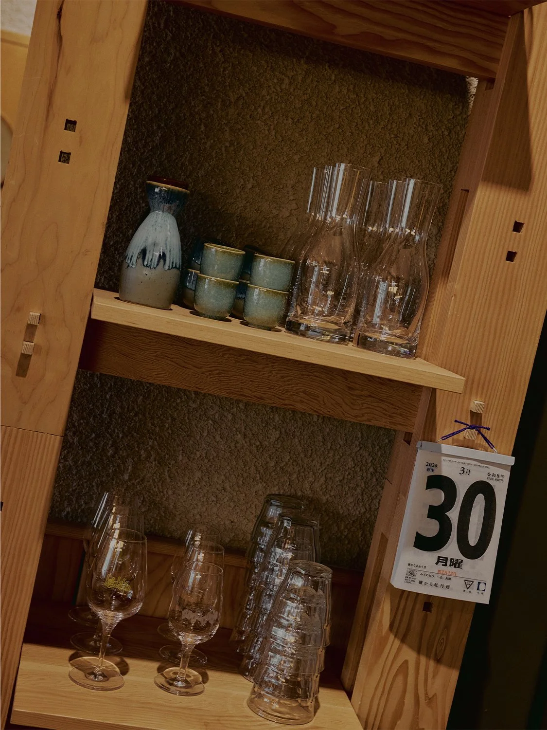 Custom wood shelving with traditional joinery displaying ceramics, glassware, and sake bottle at Hibahihi restaurant.