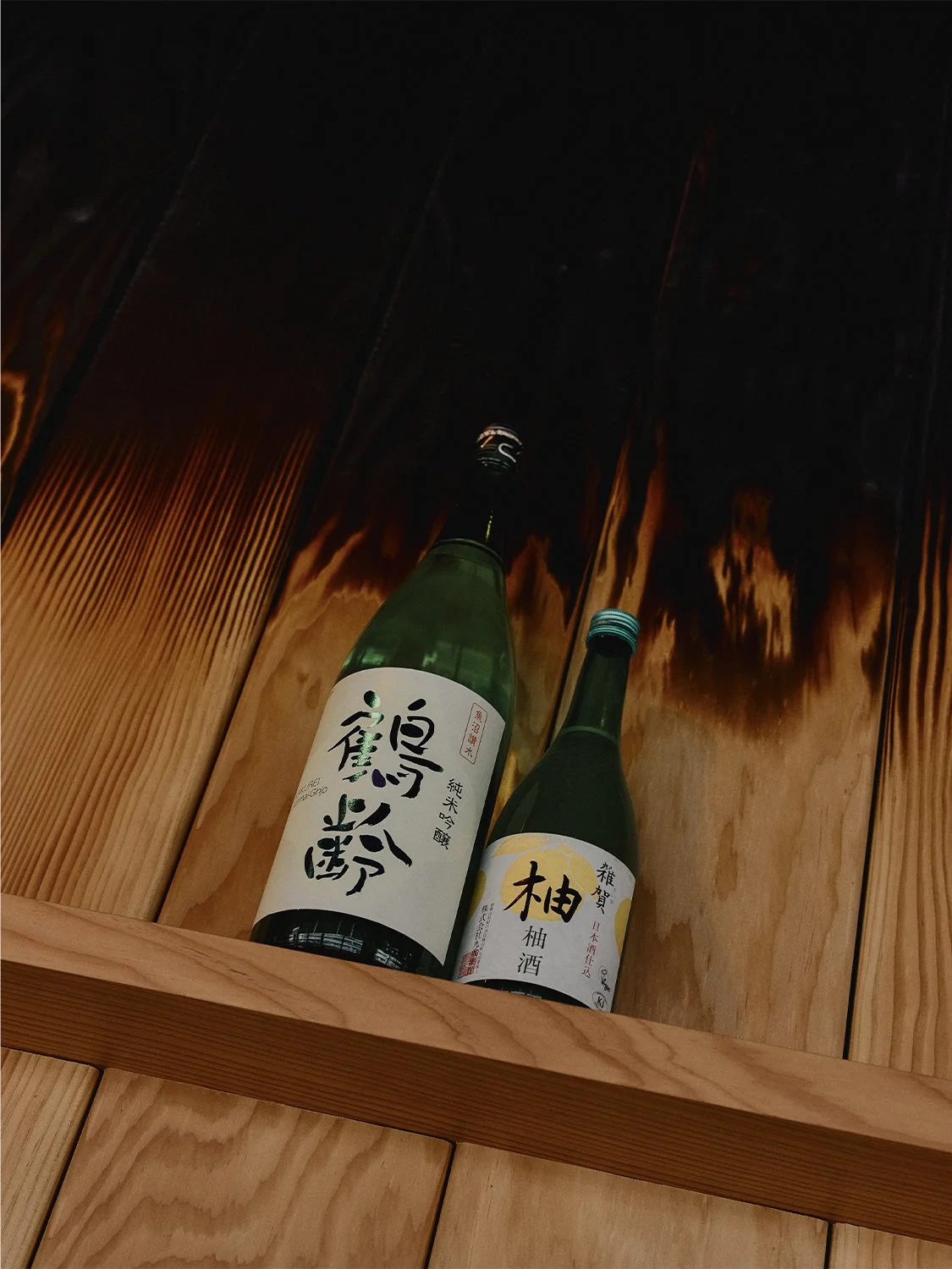 Sake bottles displayed on custom wood shelving with charred finish at Hibahihi restaurant.