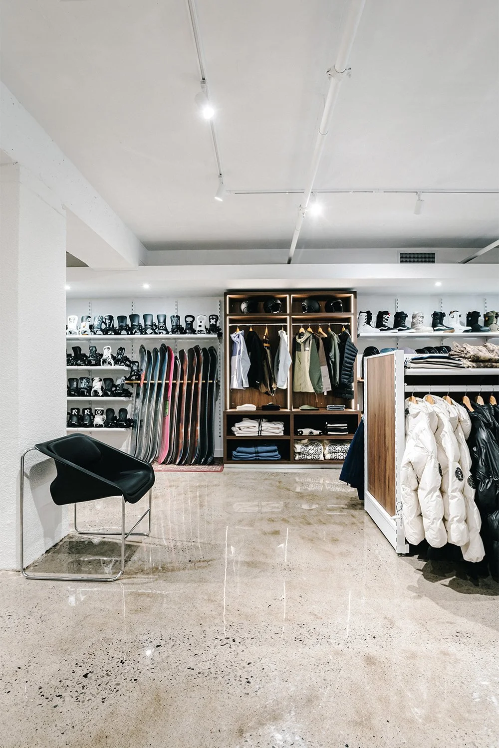 Minimal streetwear retail interior with wood shelving, clothing racks, and polished concrete floor designed by Finkel'