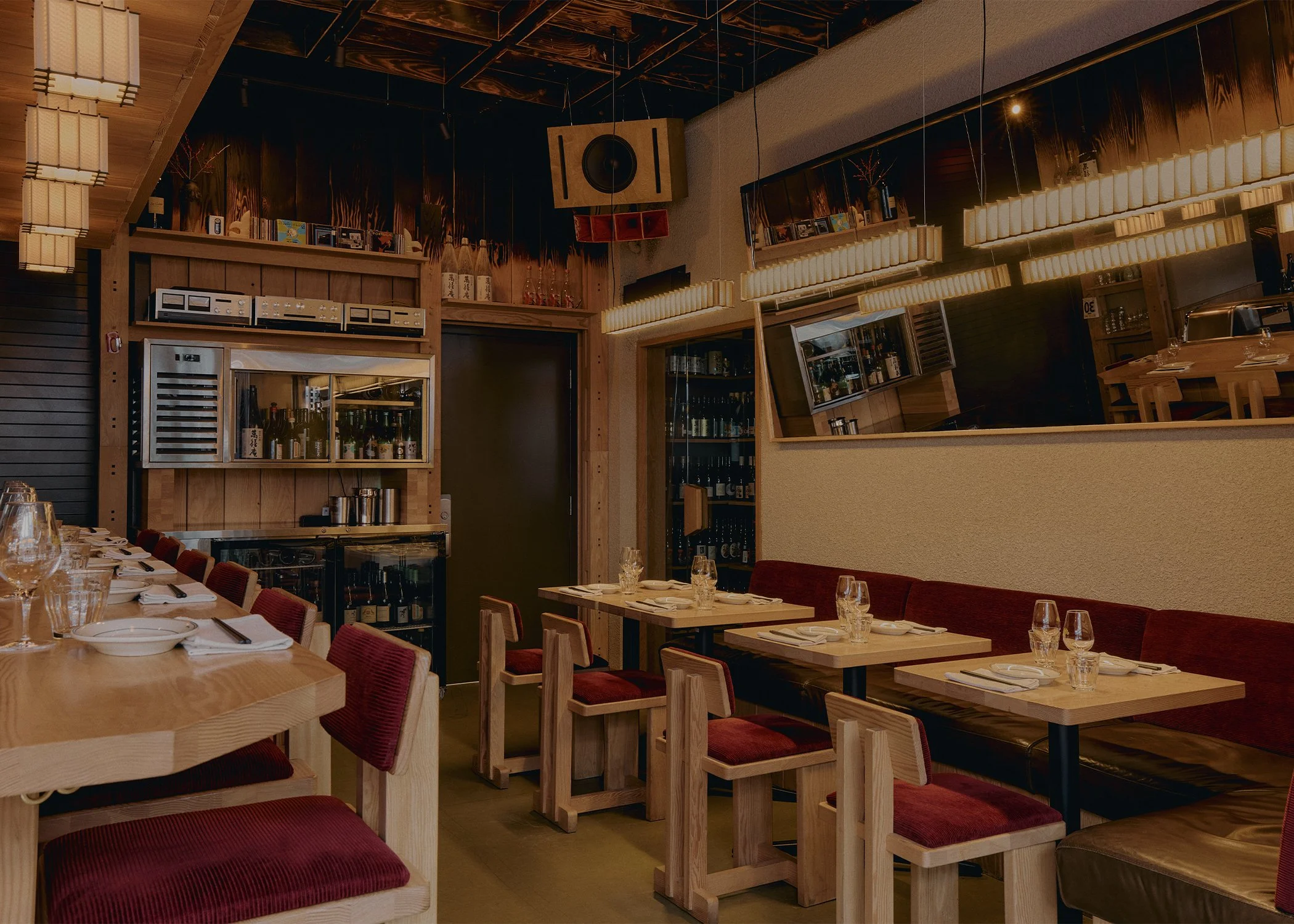Dining area at Hibahihi yakitori restaurant with custom wood tables, banquette seating, and warm pendant lighting.