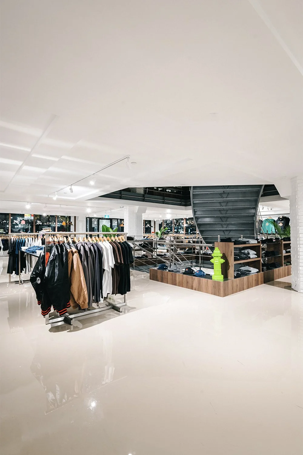 Streetwear retail interior with open floor plan, clothing racks, wood display tables, and central staircase designed by Finkel'