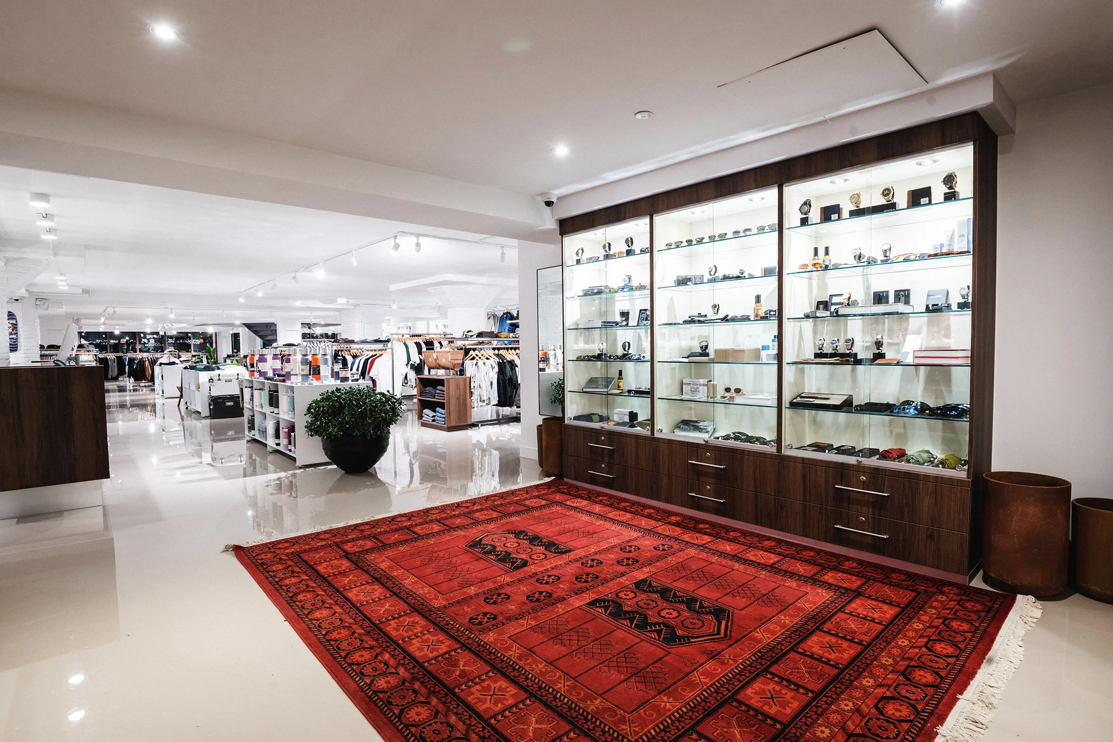 Glass display cabinets with wood framing and red rug inside a contemporary streetwear retail interior designed by Finkel'