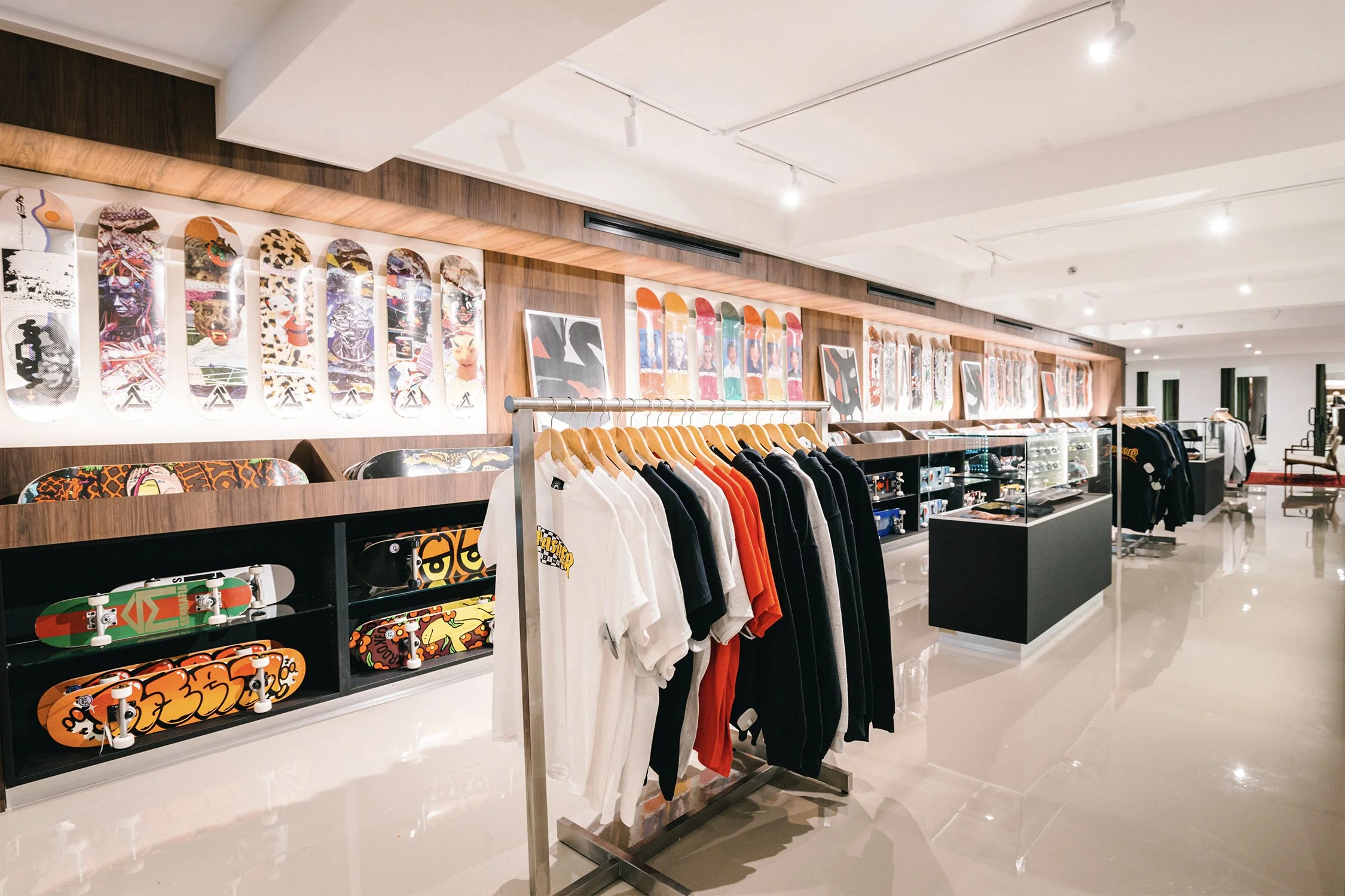 Custom wood skateboard display wall with integrated shelving and apparel racks in a contemporary retail interior designed by Finkel'