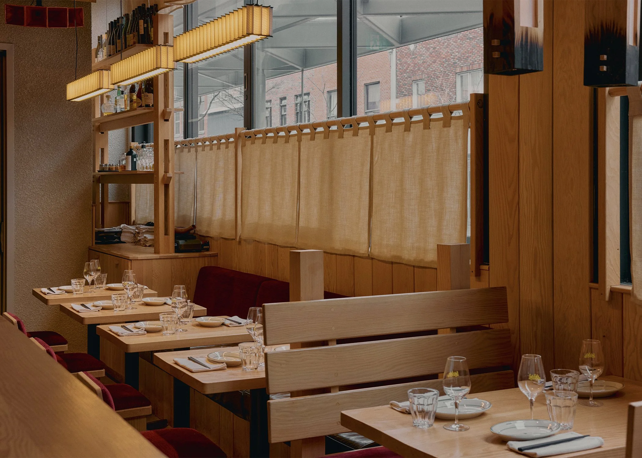 Dining area at Hibahihi with custom-designed and built wood seating by Finkel, linen window screens, and soft ambient lighting.