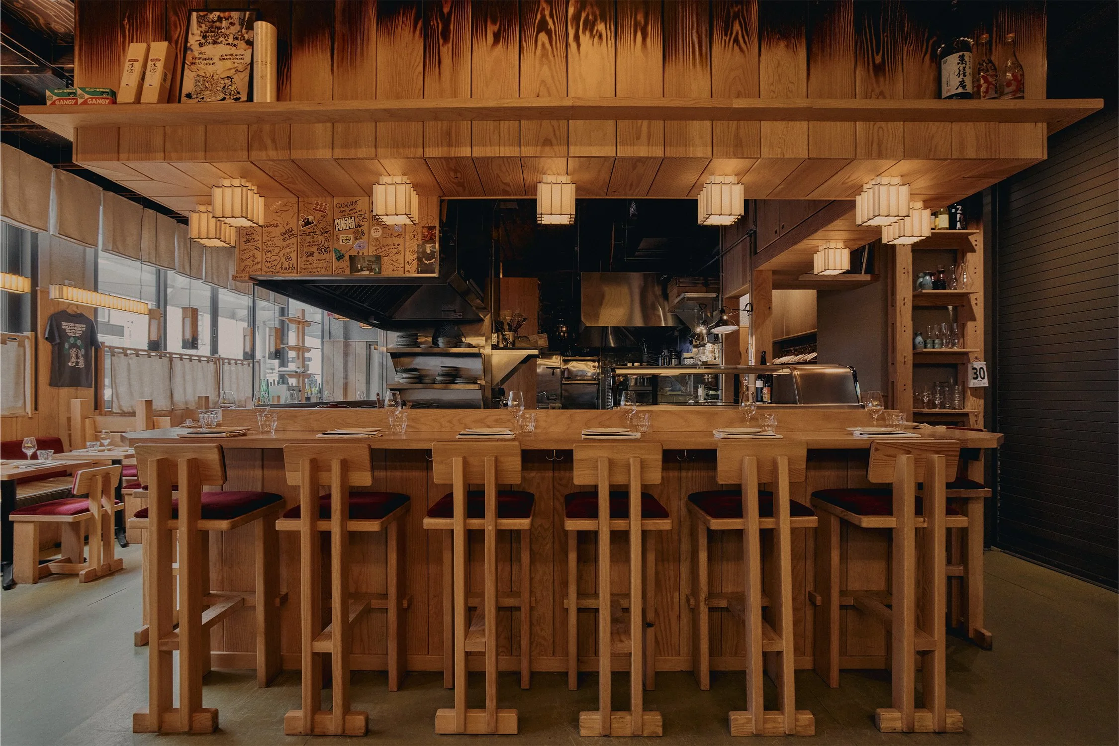 Hibahihi yakitori restaurant interior with open kitchen, custom wood furniture, and warm pendant lighting.