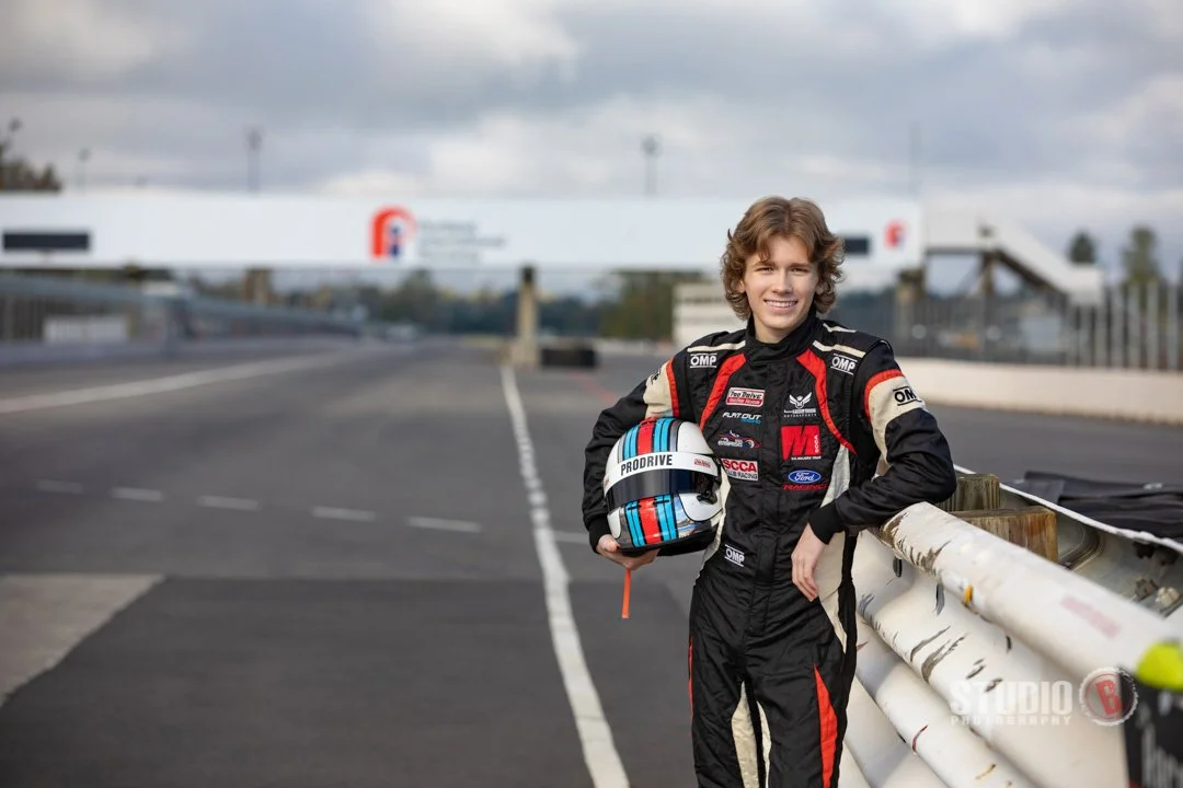 High school senior portrait at race track with racing suit and helmet - unique destination senior photography by Studio B Photography Portland Oregon