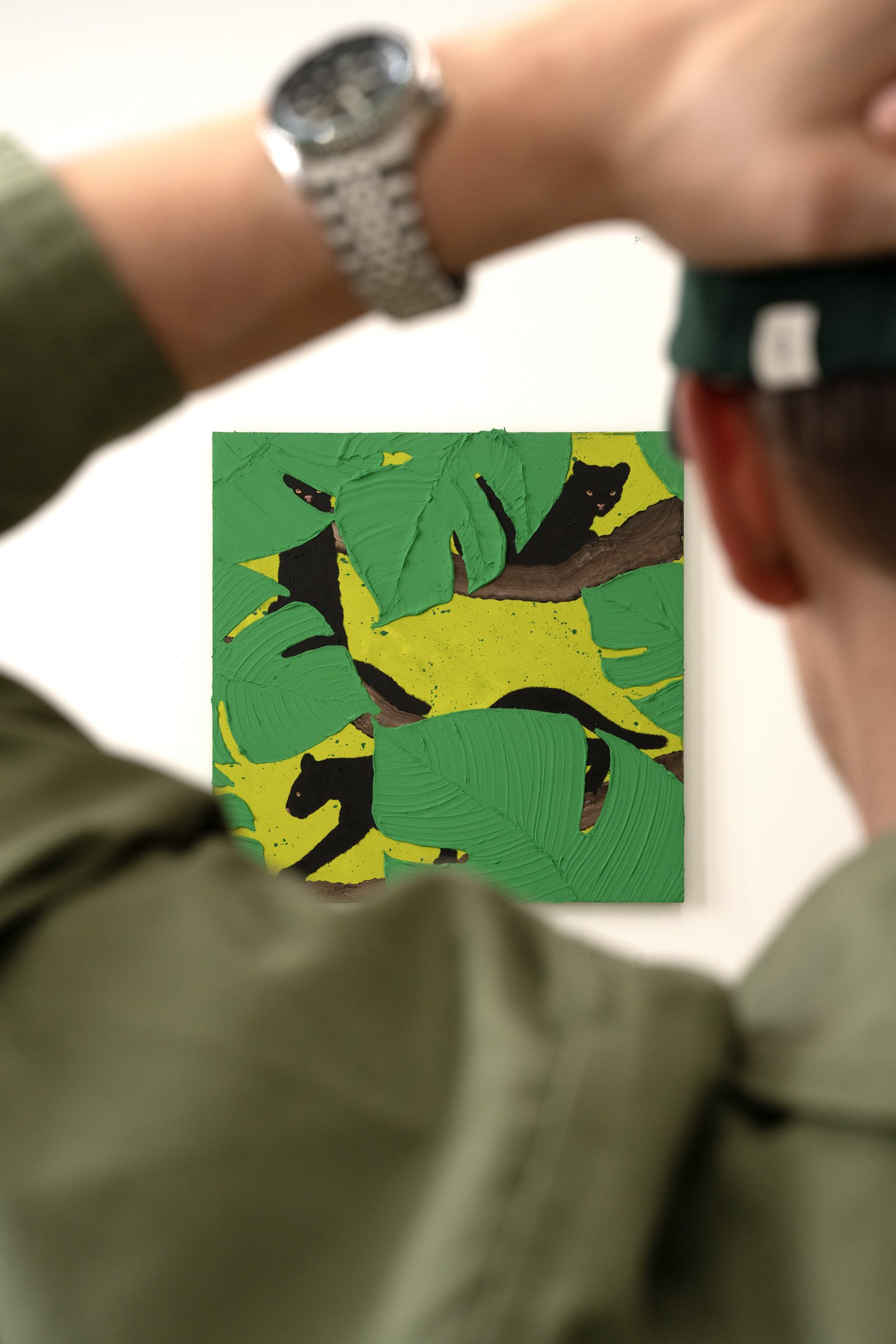 Painted black panthers peeking through tropical leaves, showcasing playful composition and vibrant contemporary color palette by Josh Brown with the artist in the foreground..