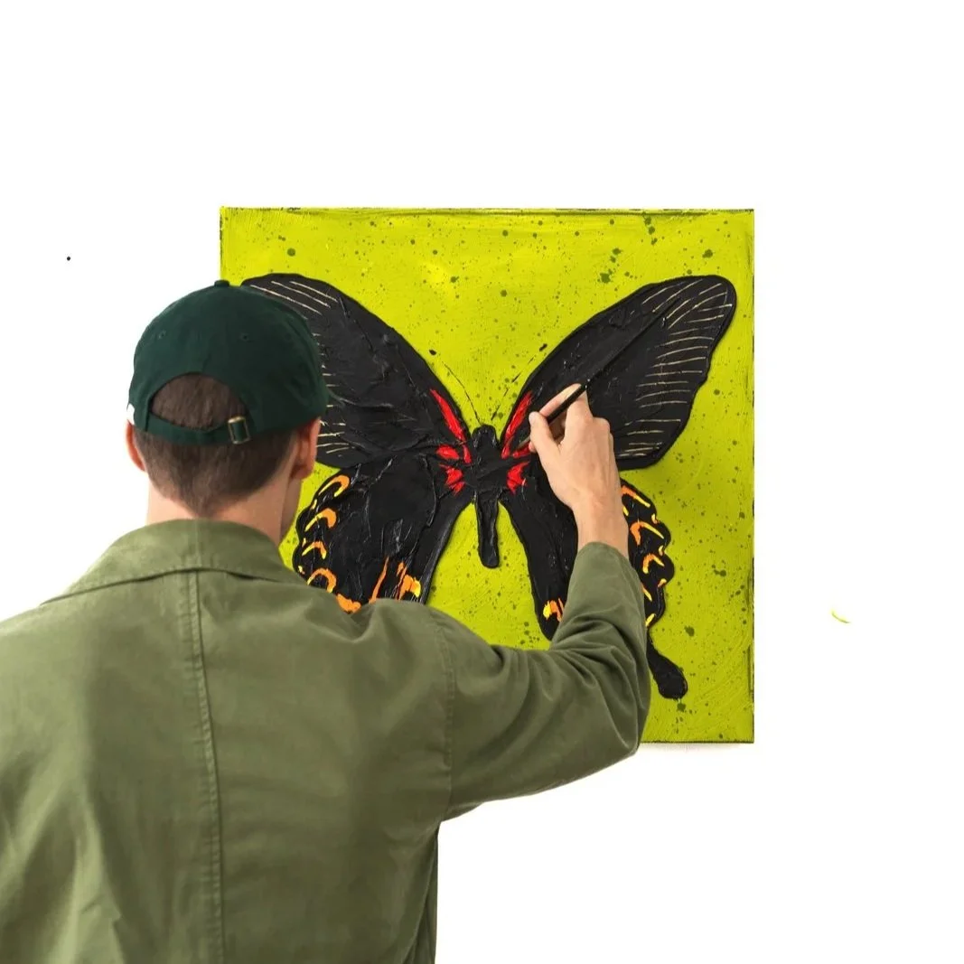 An image of the artist working on a painting of butterfly wings showing orange and yellow markings in a bold contemporary painting by Josh Brown.