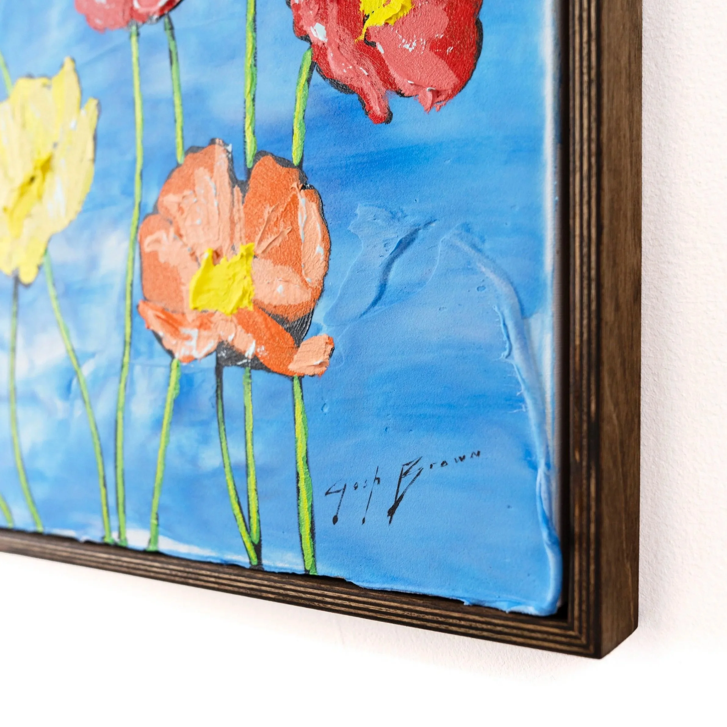 Gallery-style installation photo of a framed floral painting on a white wall demonstrating thick layers of paint, vibrant colors, and the artist's signature by Josh Brown.