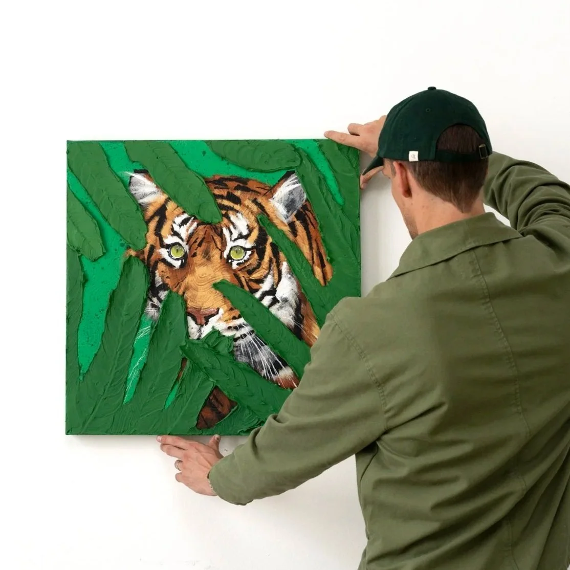 An image of the artist adjusting a painting of textured green brushstrokes surrounding a tiger’s striped face in a modern animal painting by Josh Brown.