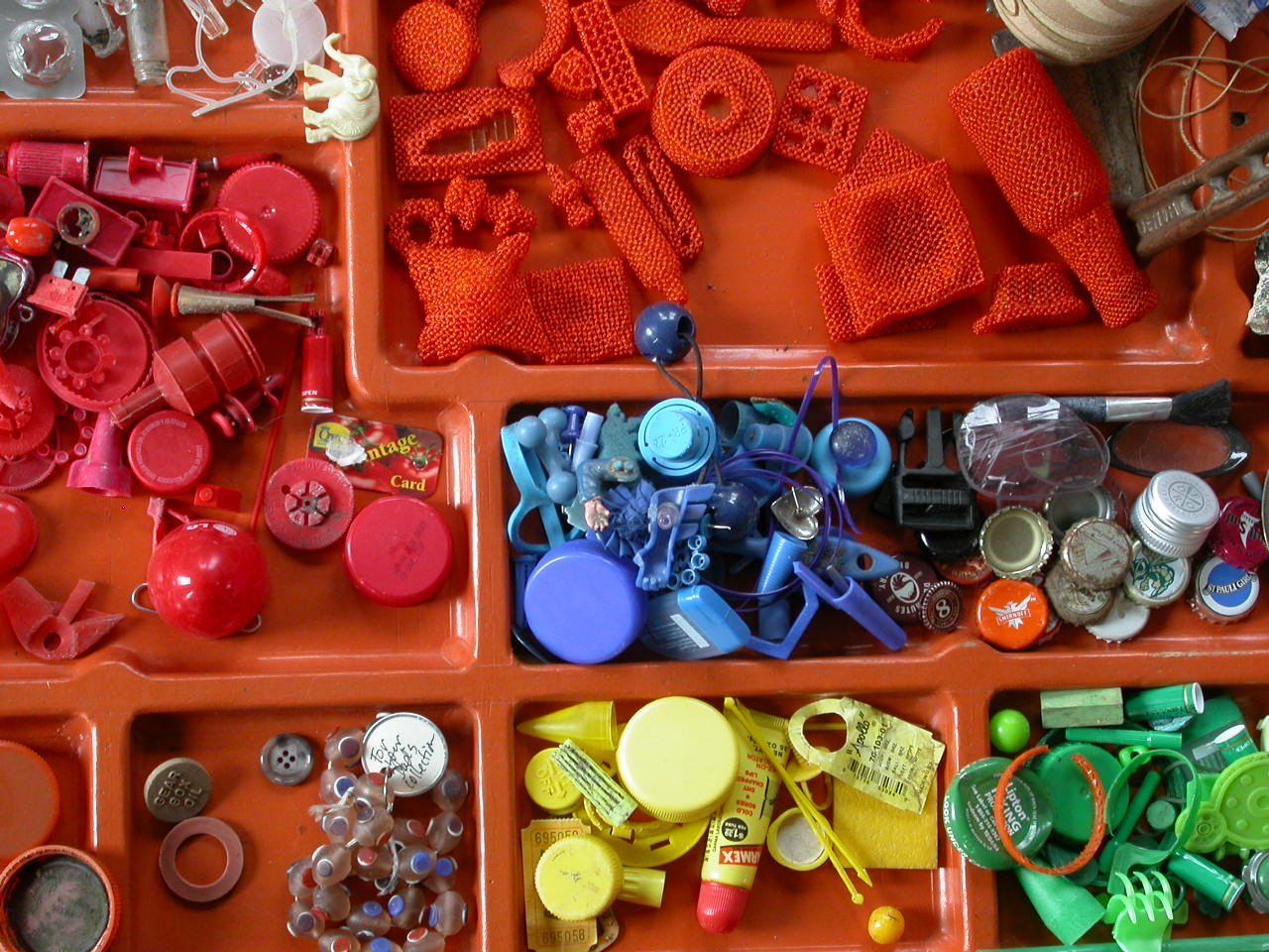 A collection of small plastic and rubber objects in colored sections, including red, blue, yellow, and green items like caps, caps, clips, and toys.