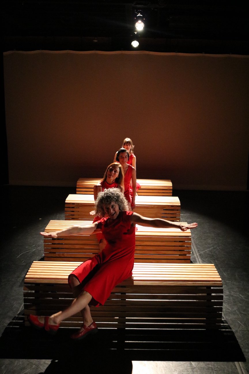 Four women in red dresses in motion around several wooden benches that constantly shift to change the stage picture. Emotions vary from fear to desire, and subdued contemplation to elated giddiness.