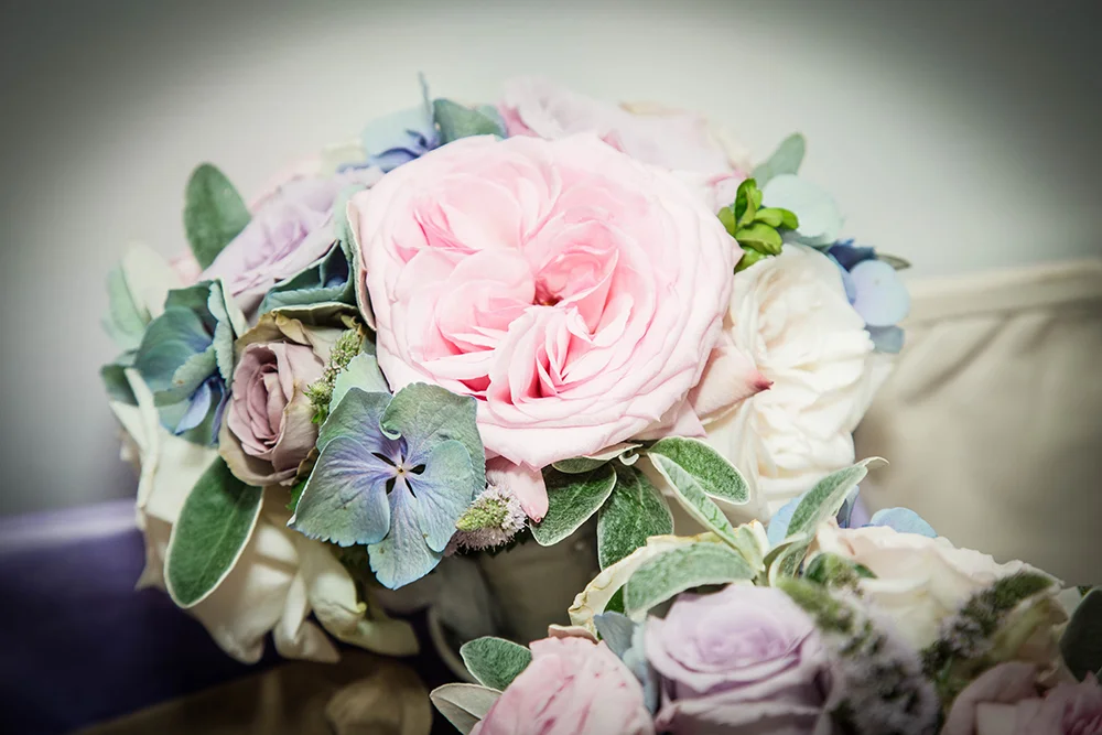 A bouquet of pink, white, and purple flowers, including roses and hydrangeas, with green leaves.