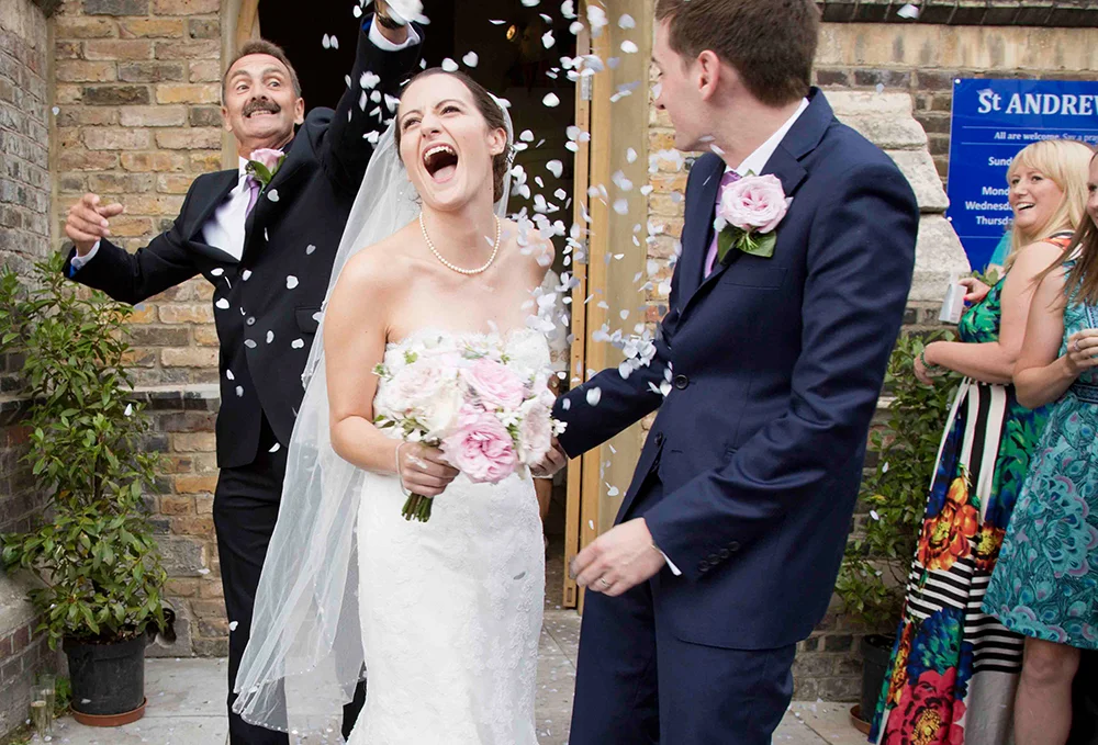 A joyful bride and groom celebrating their wedding outside, surrounded by friends throwing confetti.