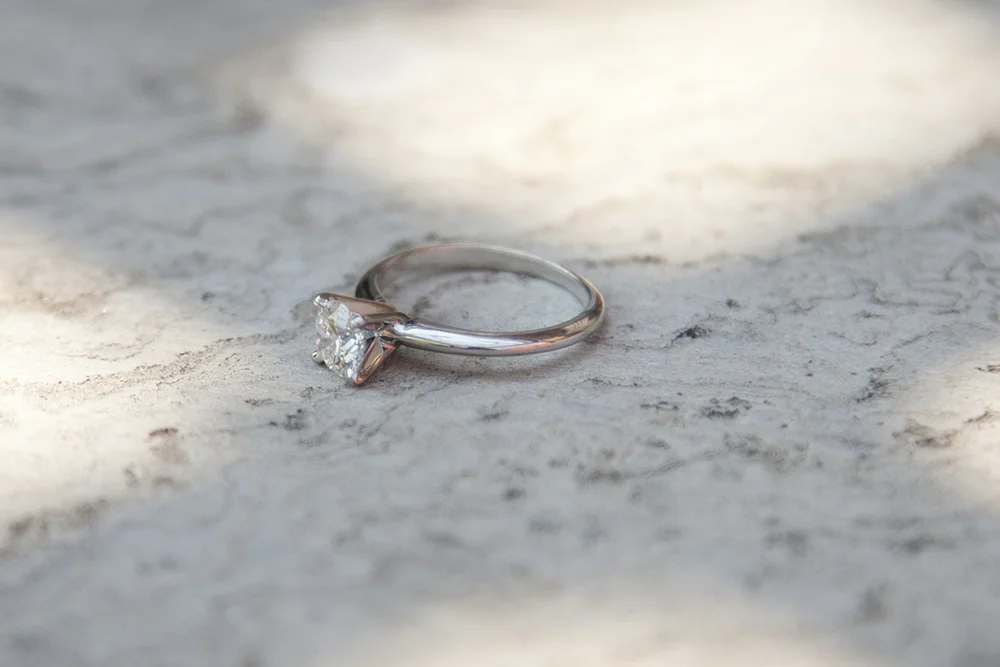 A silver engagement ring with a large diamond solitaire on a textured surface with soft lighting.