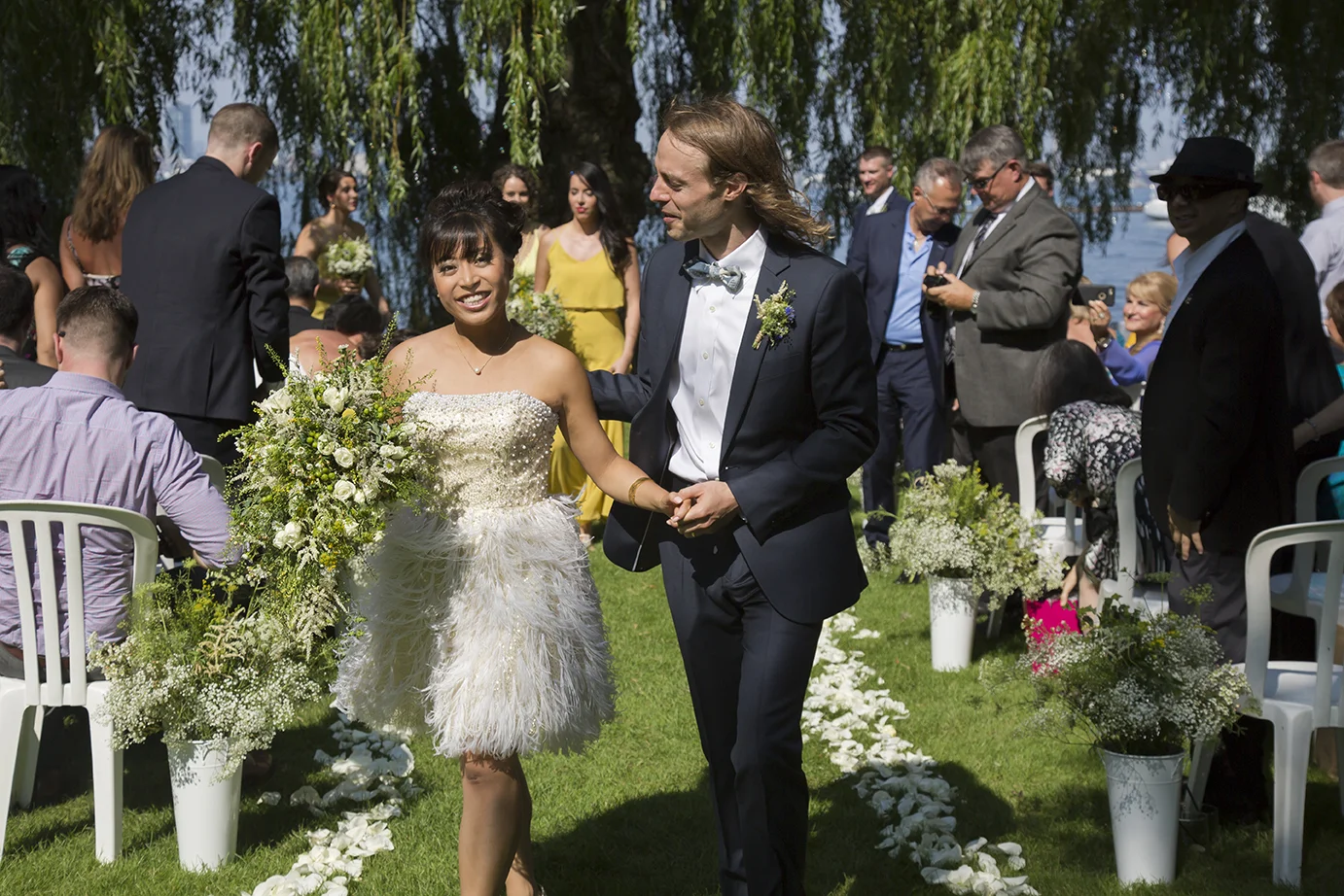 Bride and groom walking down aisle during outdoor wedding ceremony with wedding guests watching and taking photos.