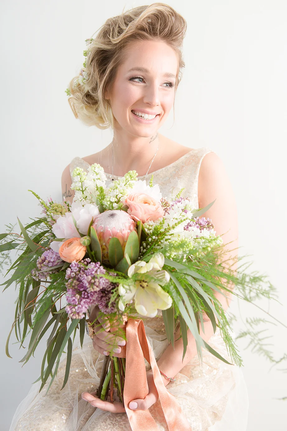 A smiling woman in a wedding dress holding a large bouquet of flowers.