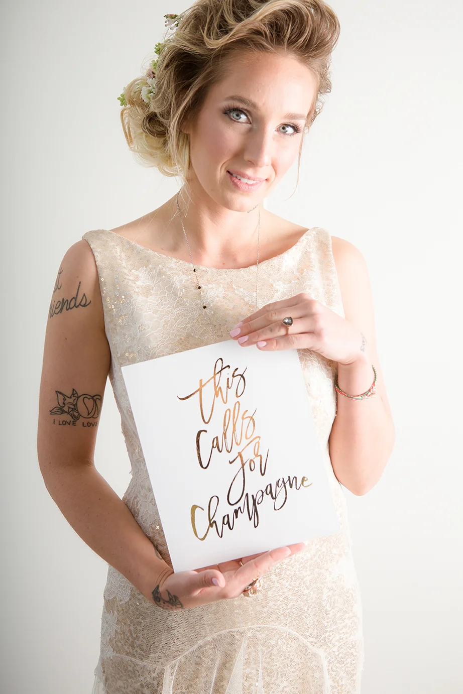 A woman in a lace dress with styled hair holding a sign that says "this calls for champagne" written in calligraphy.