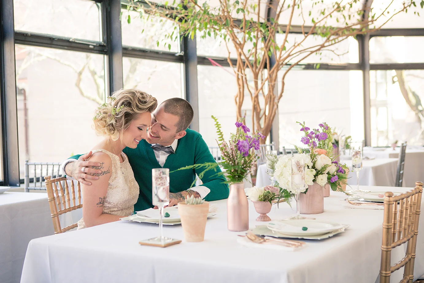 A couple sitting at a decorated table in a bright room, smiling and leaning close to each other.