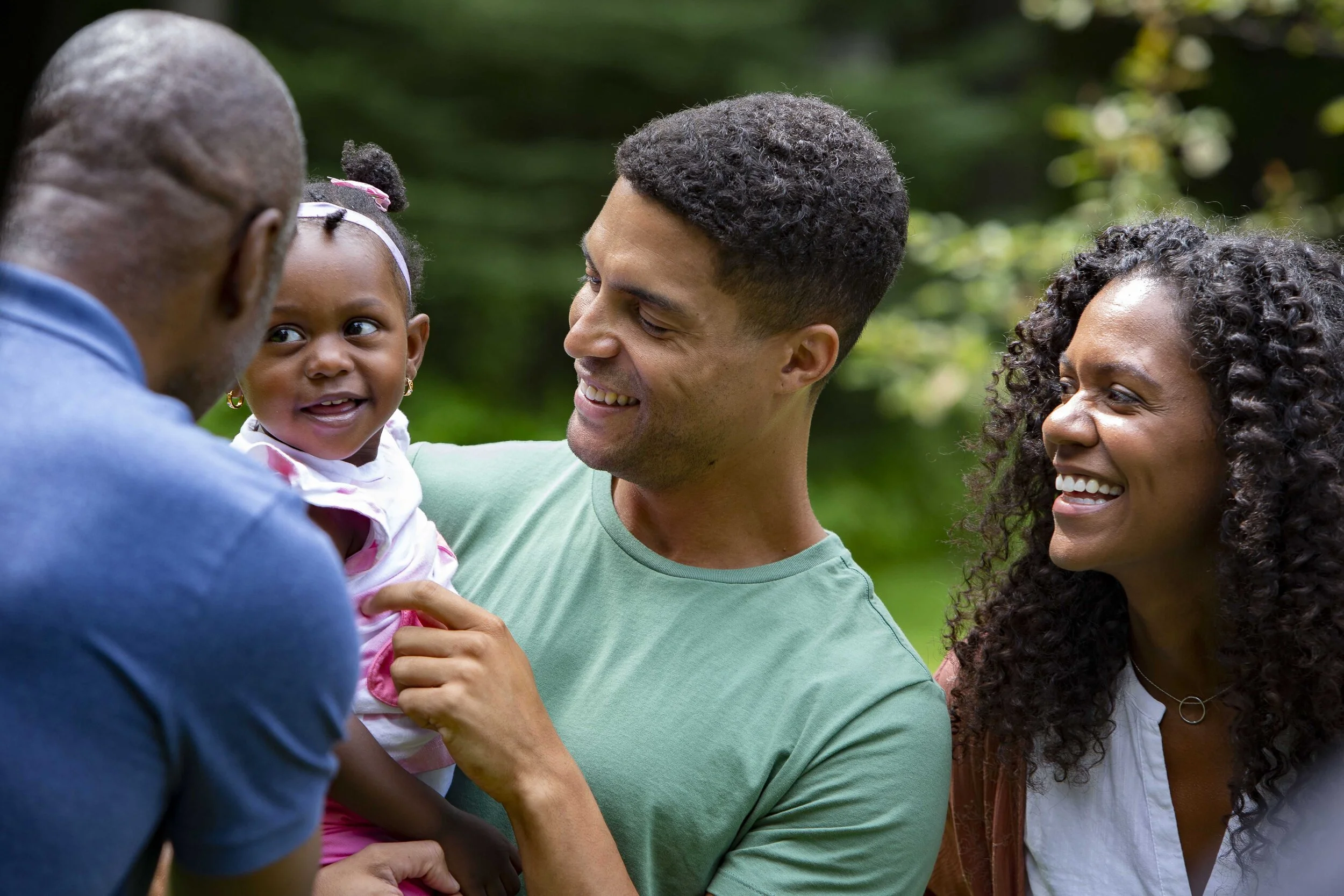 A family enjoying time outdoors, with a man holding a young girl while an older man and woman smile nearby.