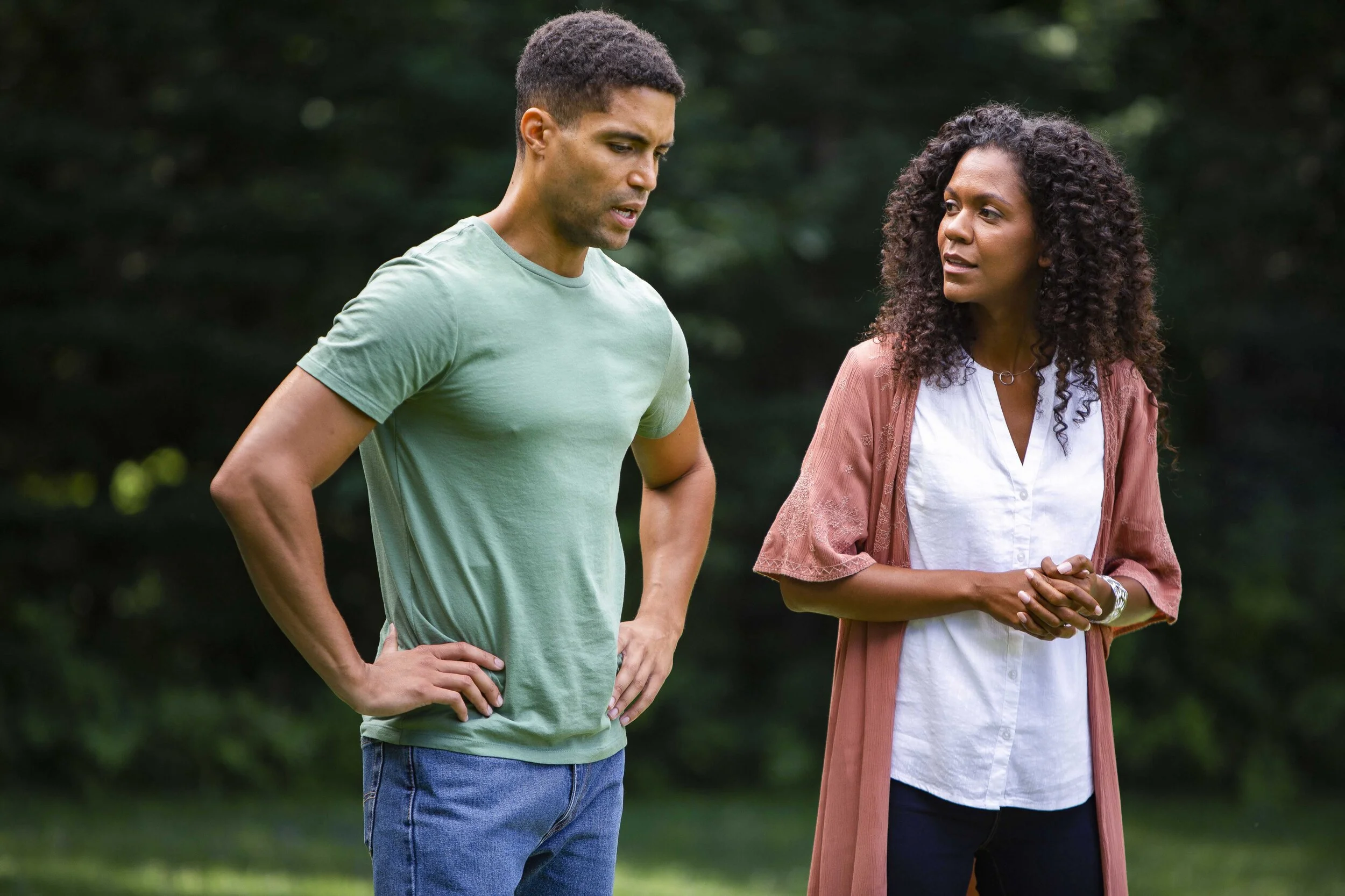 A man and a woman having a serious conversation outdoors in a park-like setting.