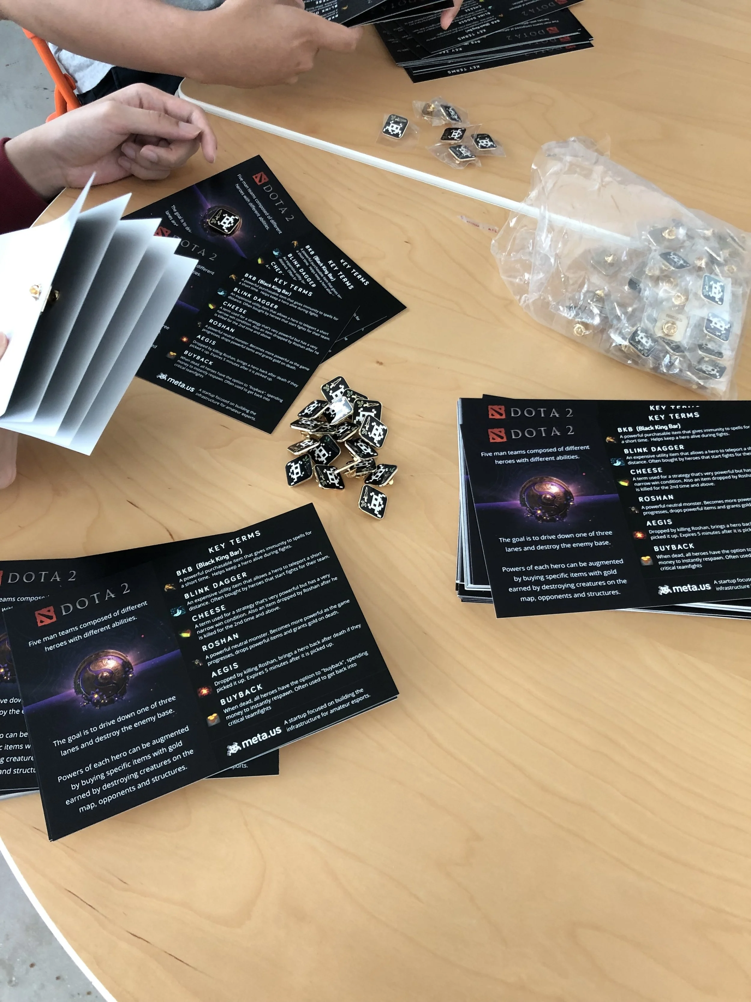 Table with pamphlets and small tiles with a Dota 2 themed game setup, including instructions, game pieces, and promotional material.