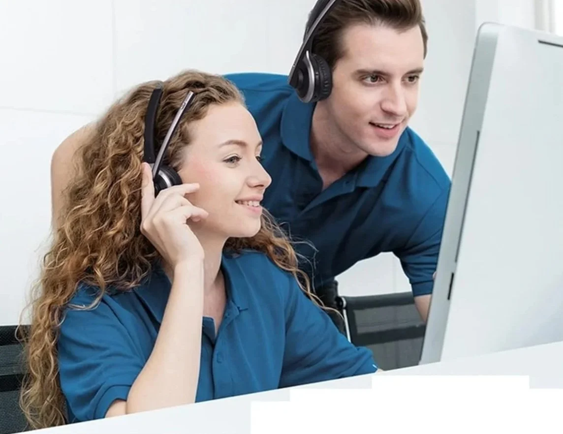 A woman and a man wearing headphones looking at a computer monitor together, smiling.