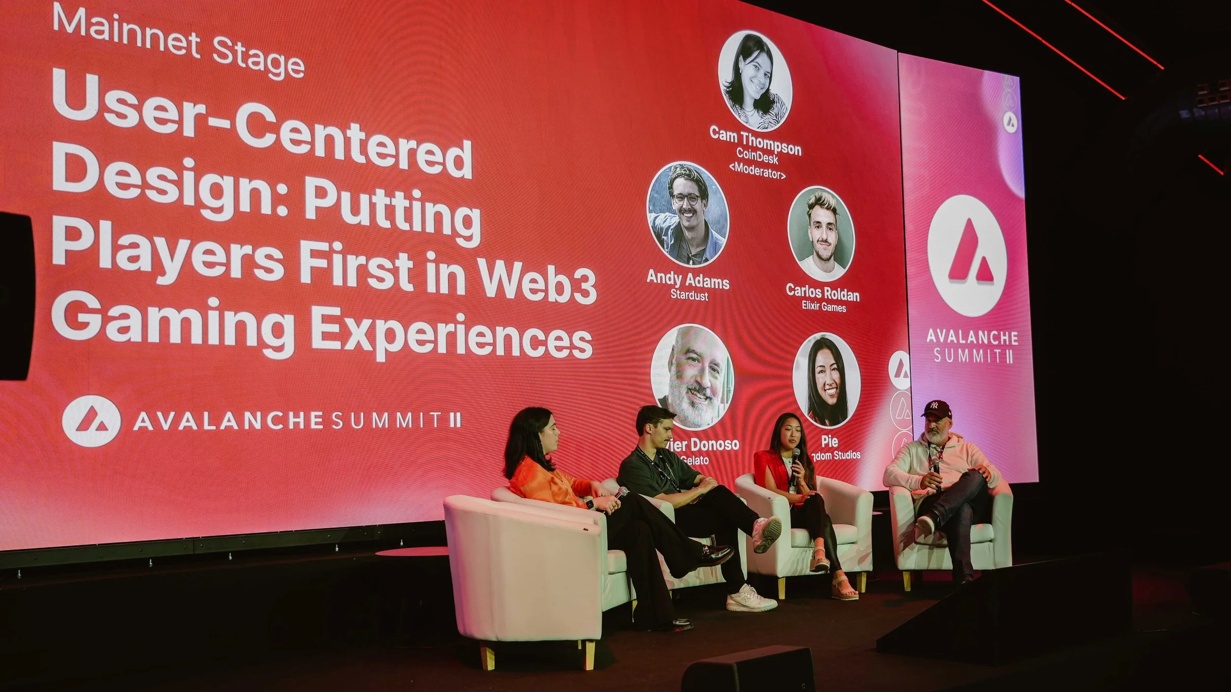 A panel discussion at Avalanche Summit II with four speakers seated on stage in front of a large red screen displaying the event details and speaker names.