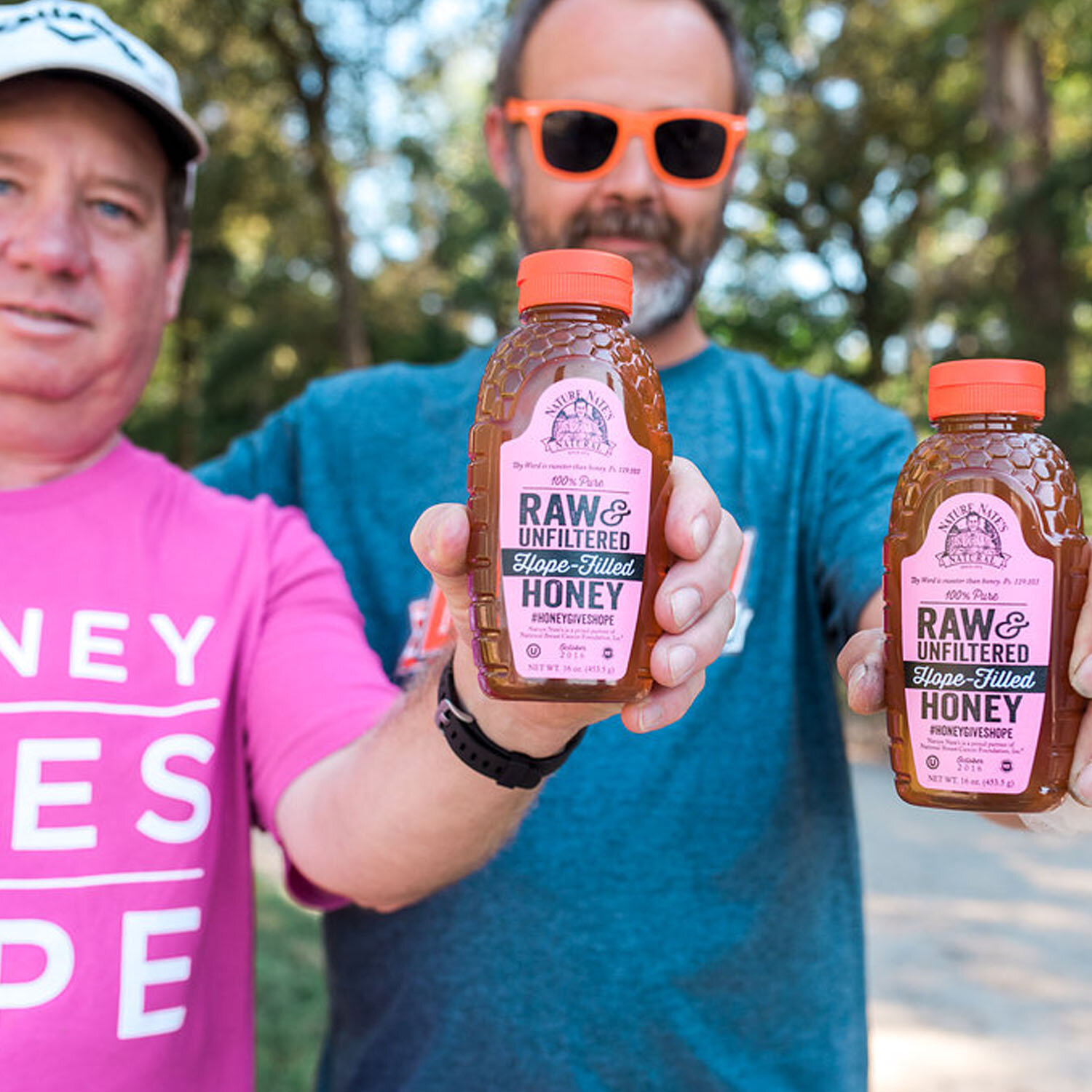 Two Nature Nate's employees holding a limited edition pink Nature Nate's 16oz honey bottles designed to support the Honey Gives Hope corporate giveback program