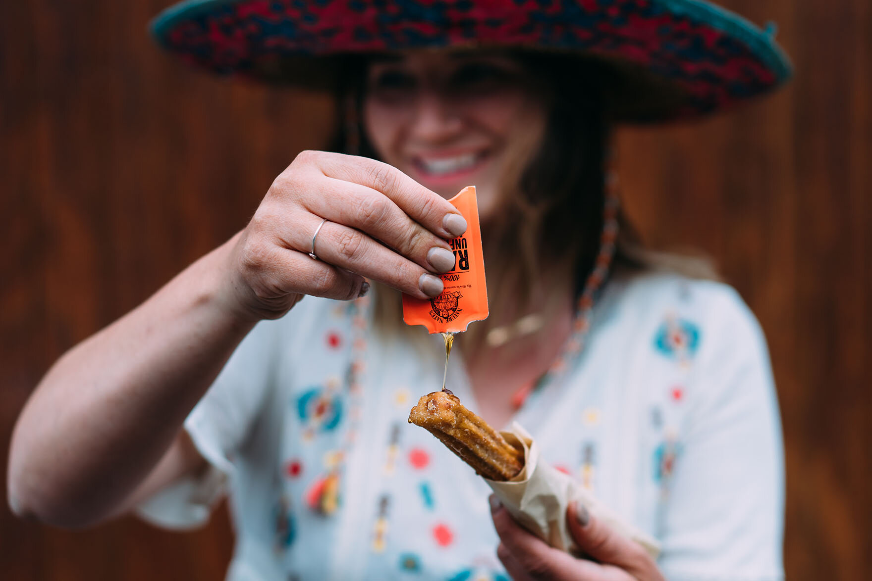 Smiling woman wearing a sombrero drizzling honey from a Nature Nate's honey packet on a homemade churro