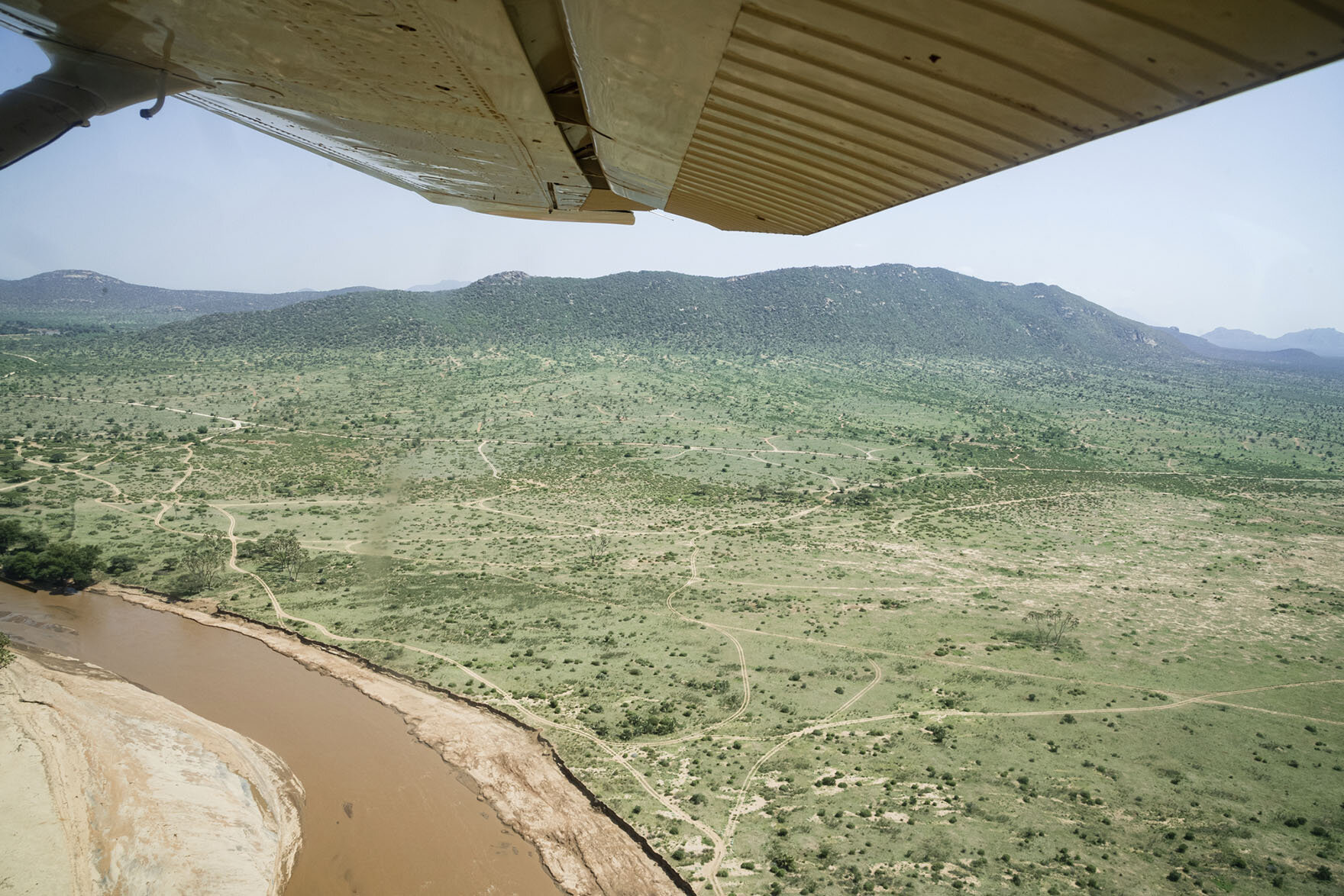  Panoramic view of the Masai Mara from a single engine plane flying over a mountainous river valley 