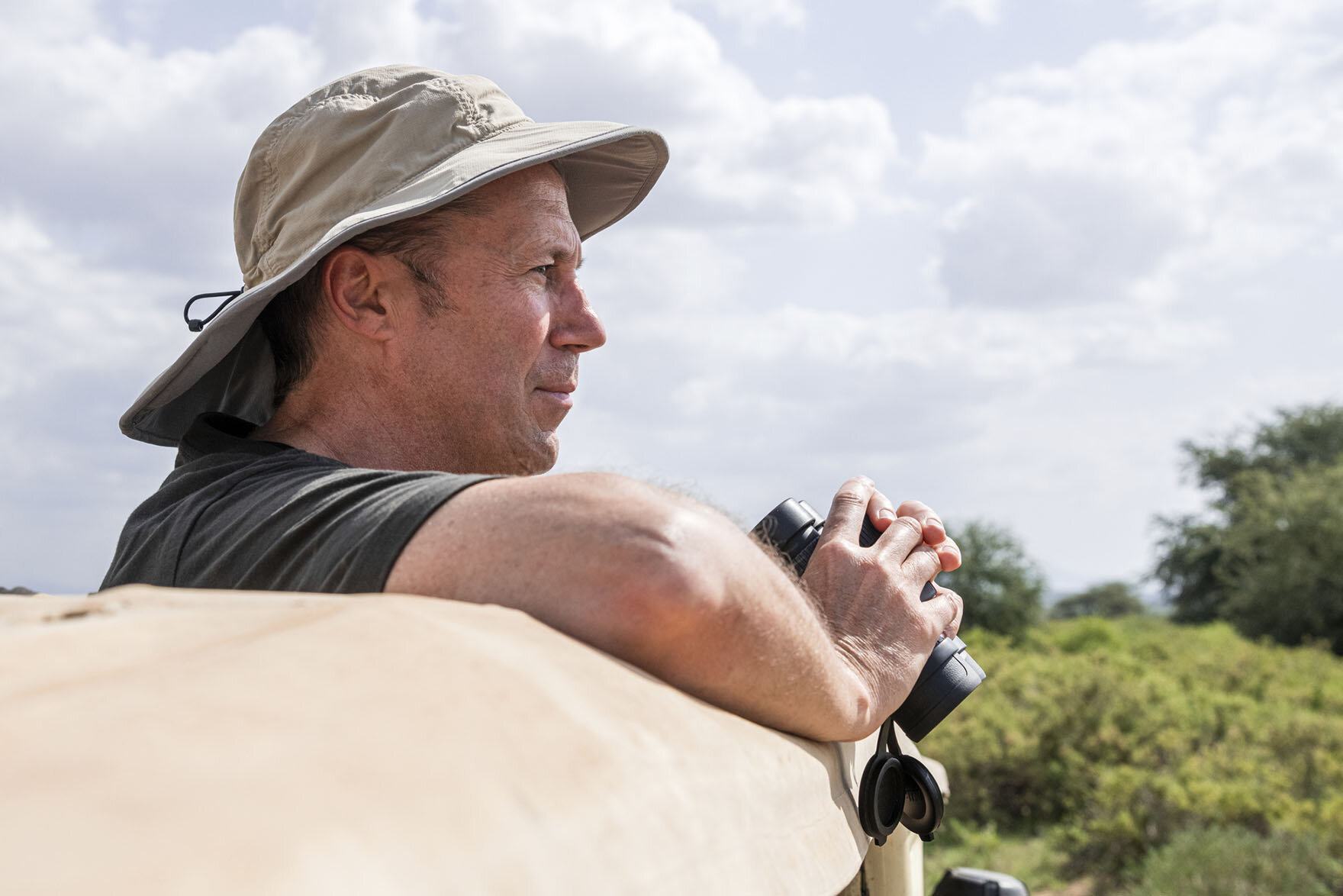 Curt Vander Meer peeking out the top of a jeep with binoculars surveying the Masai Mara game reserve in Narok County, Kenya