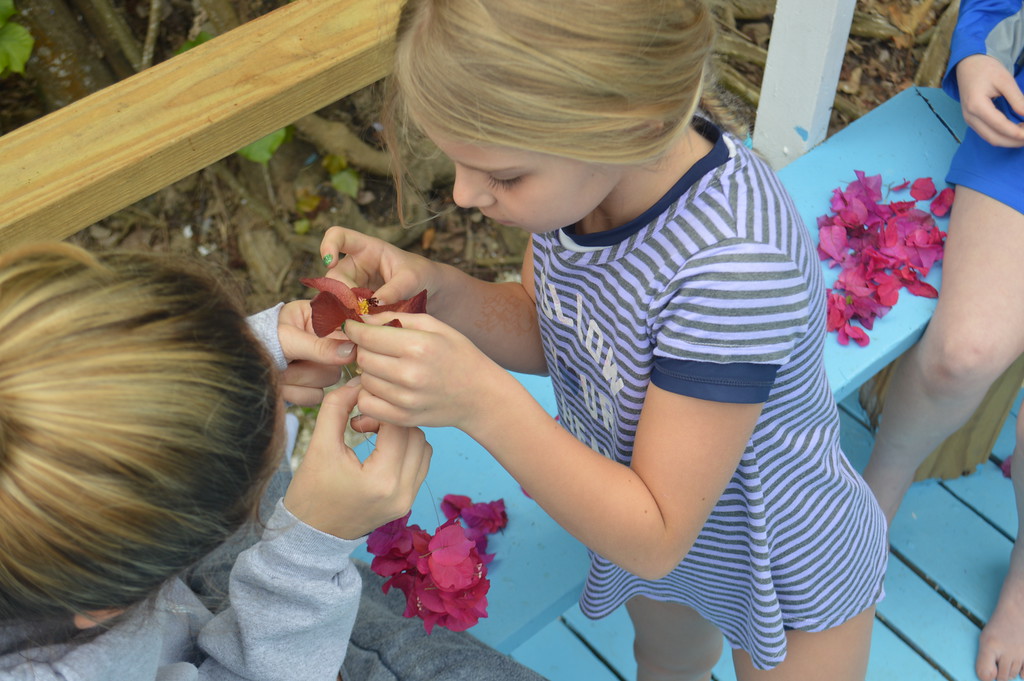 A Counselor-In-Training helps a camper create a handmade flower necklace, called a lei, to wear during her hula performance. 