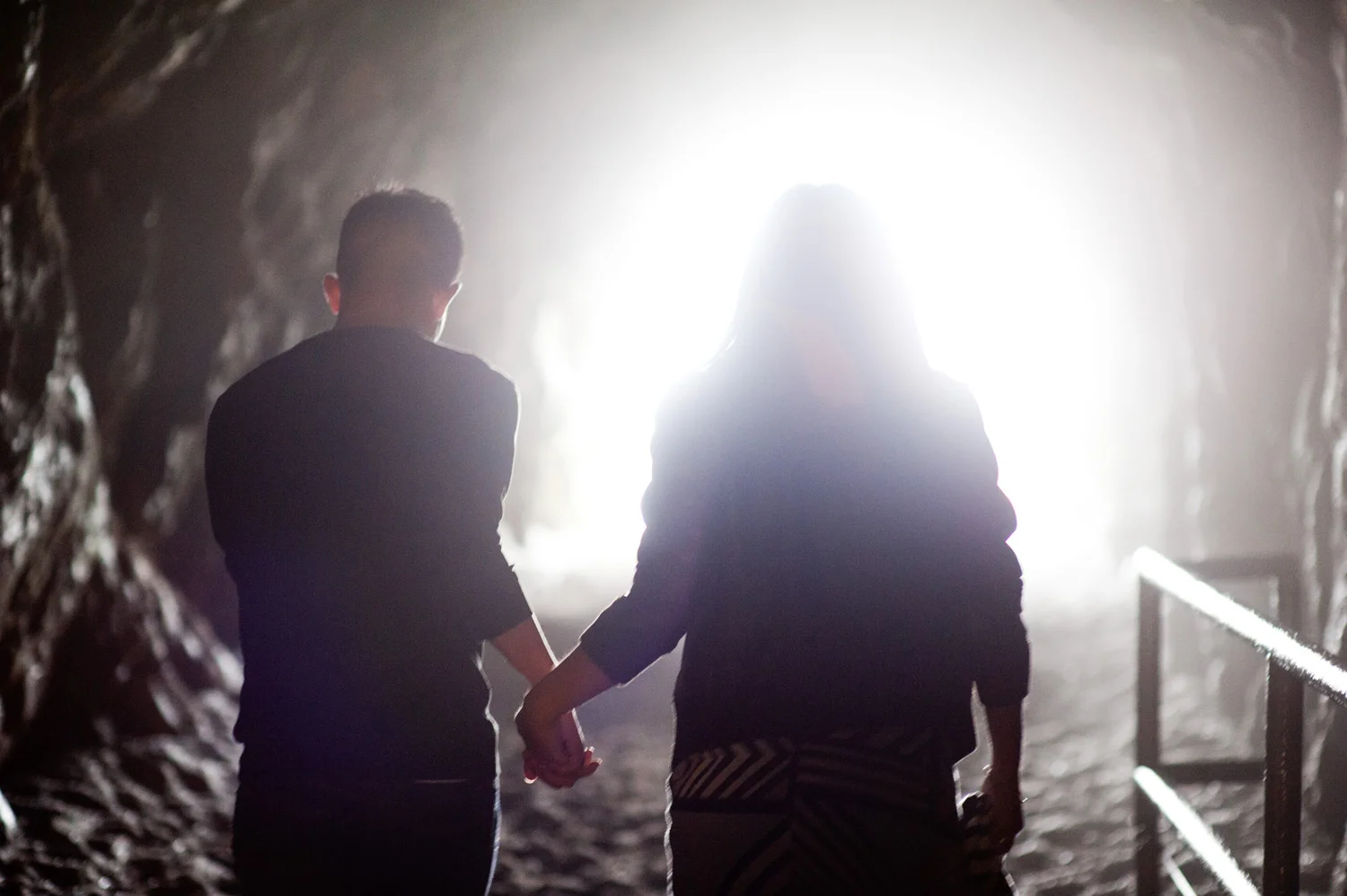 engagement photo couple holds hands and heads into the light at the end of the tunnel