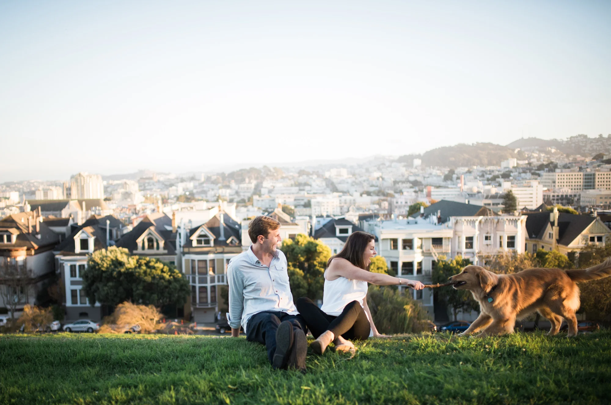 San Francisco engagement photo with couple sitting on the hill playing fetch with a dog