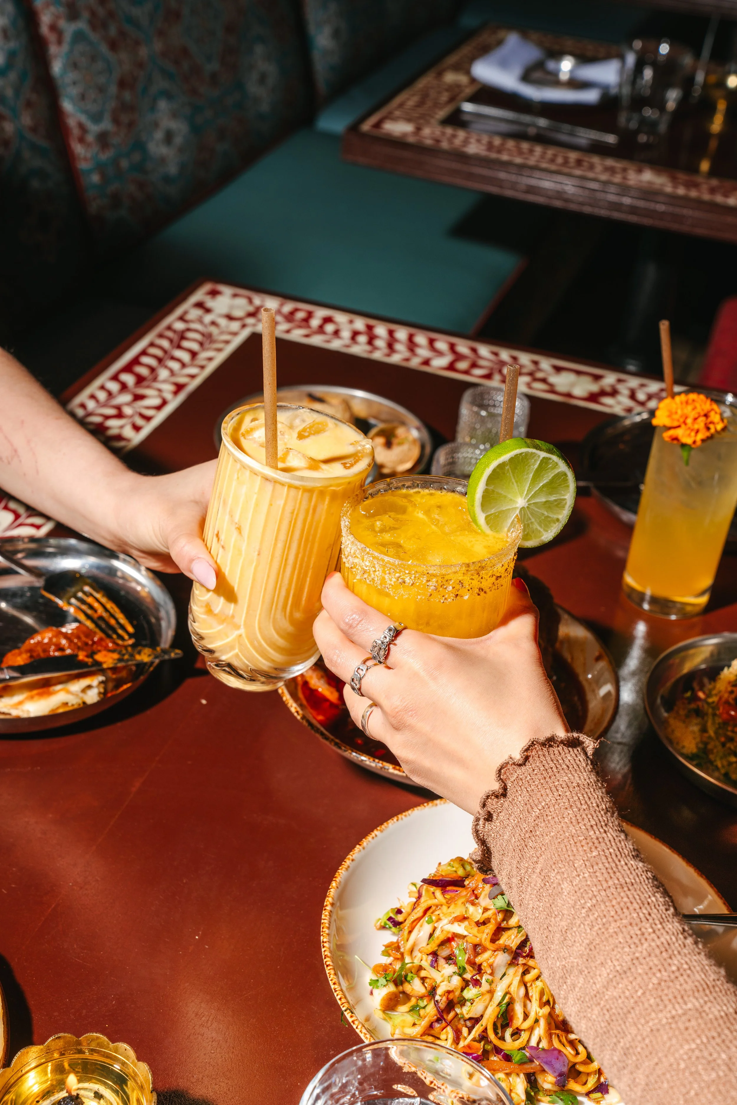 Hard light lifestyle photography in Midtown Atlanta for Indian restaurant showing two people sharing a toast with mango lassi and a margarita.