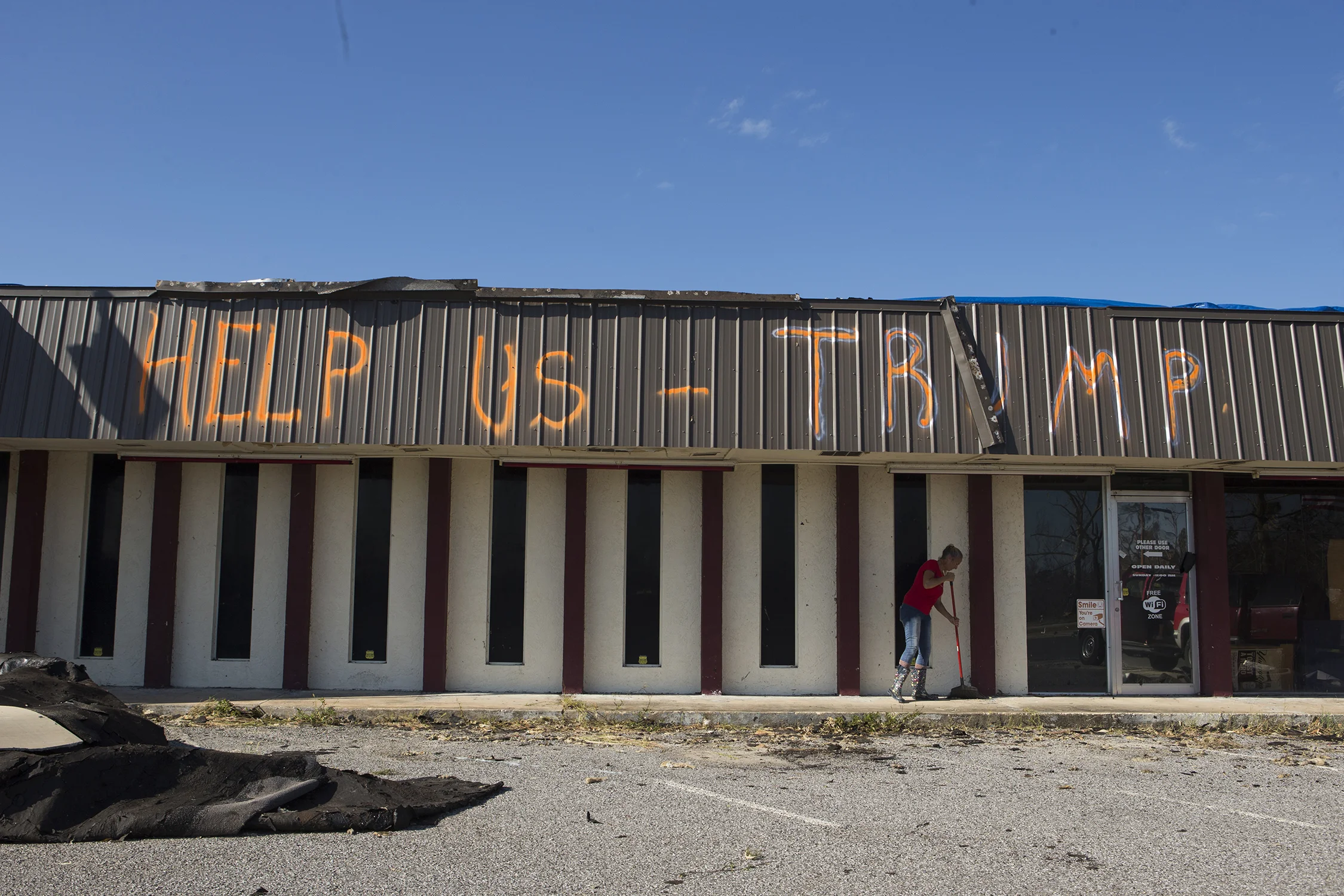  Jennifer Burton, the owner of Pockets in Parker, Florida, sweeps her front porch on Monday, October 15, 2018. Her husband painted a message for President Donald Trump near the road from Tyndall Air Force Base into Bay County. "Who's working for the 